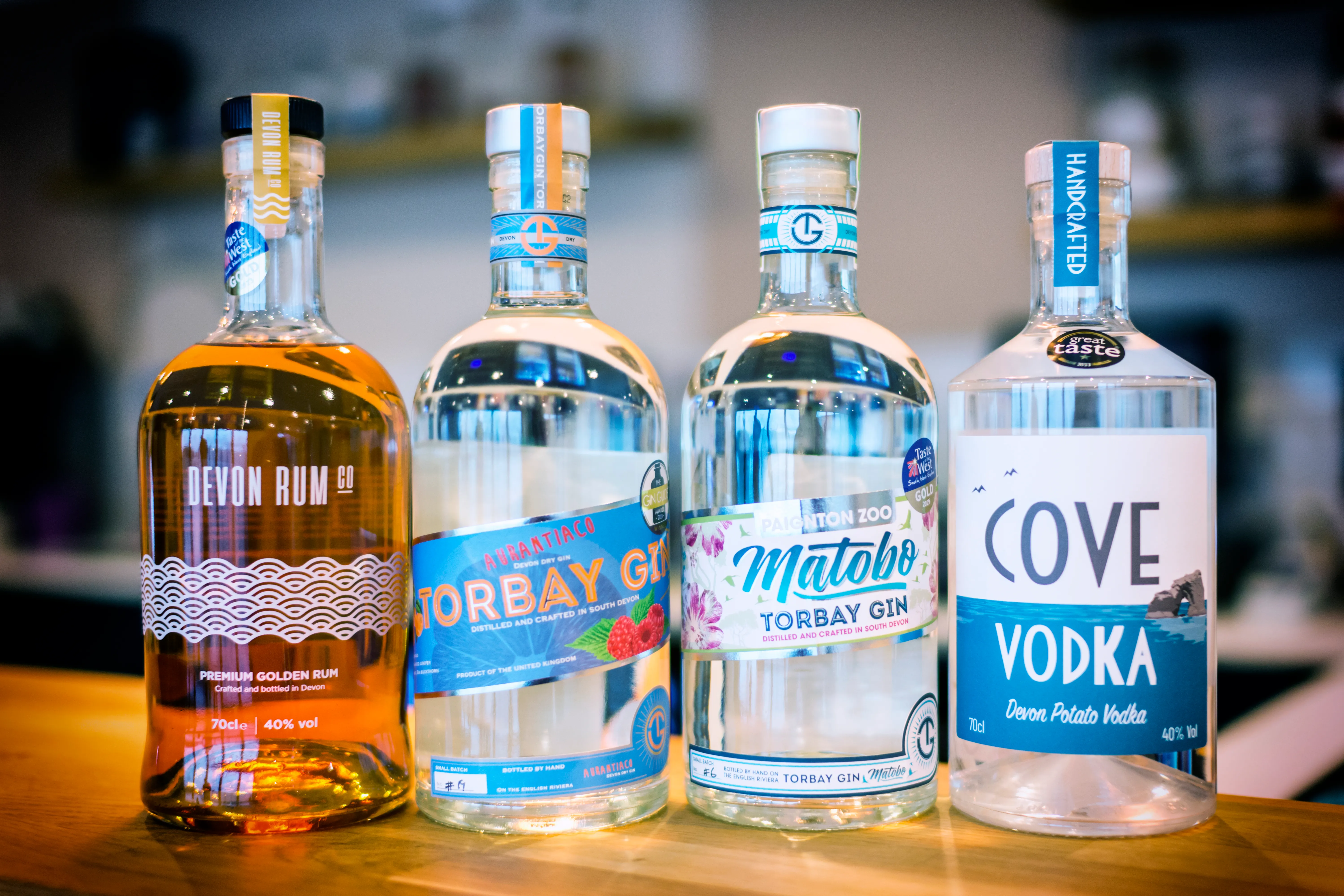 Four bottles of Devon spirits on a wooden counter, including Devon Rum Co golden rum, two Torbay gins and Cove vodka.