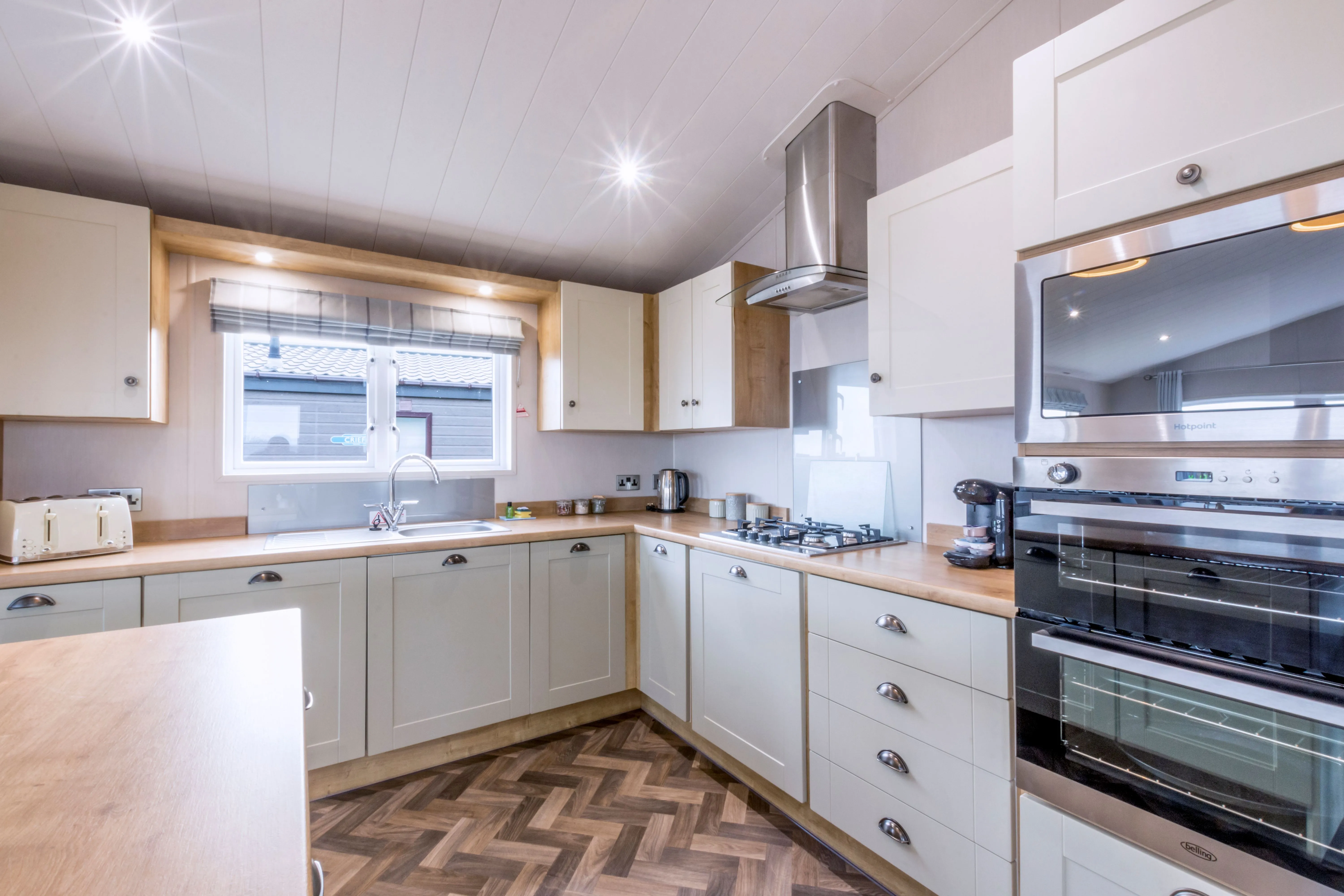 Modern fitted kitchen with cream shaker-style cabinets, wood-effect worktops, integrated double oven and gas hob