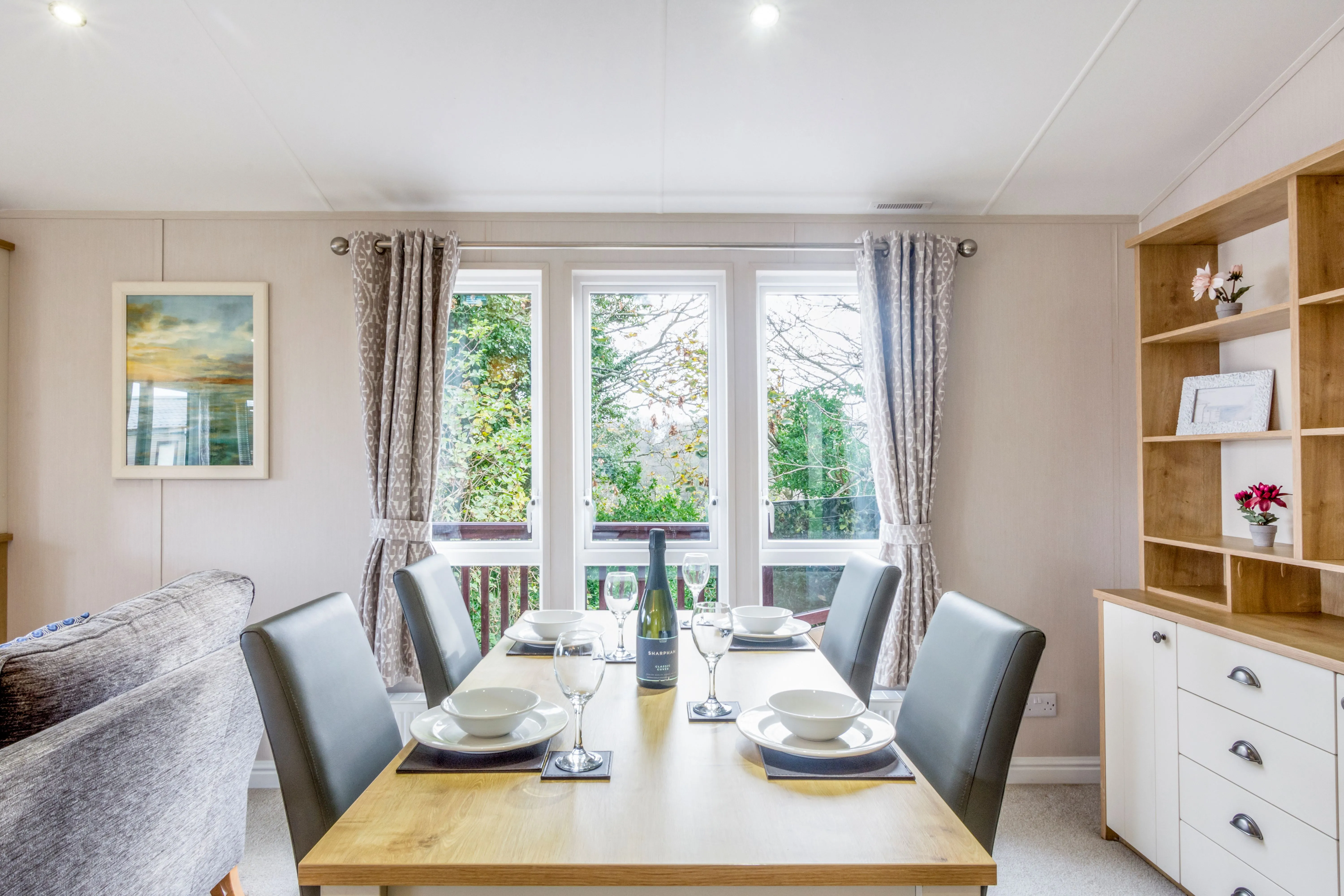 Bright dining area with a wooden table set for four beside large windows and built-in shelving