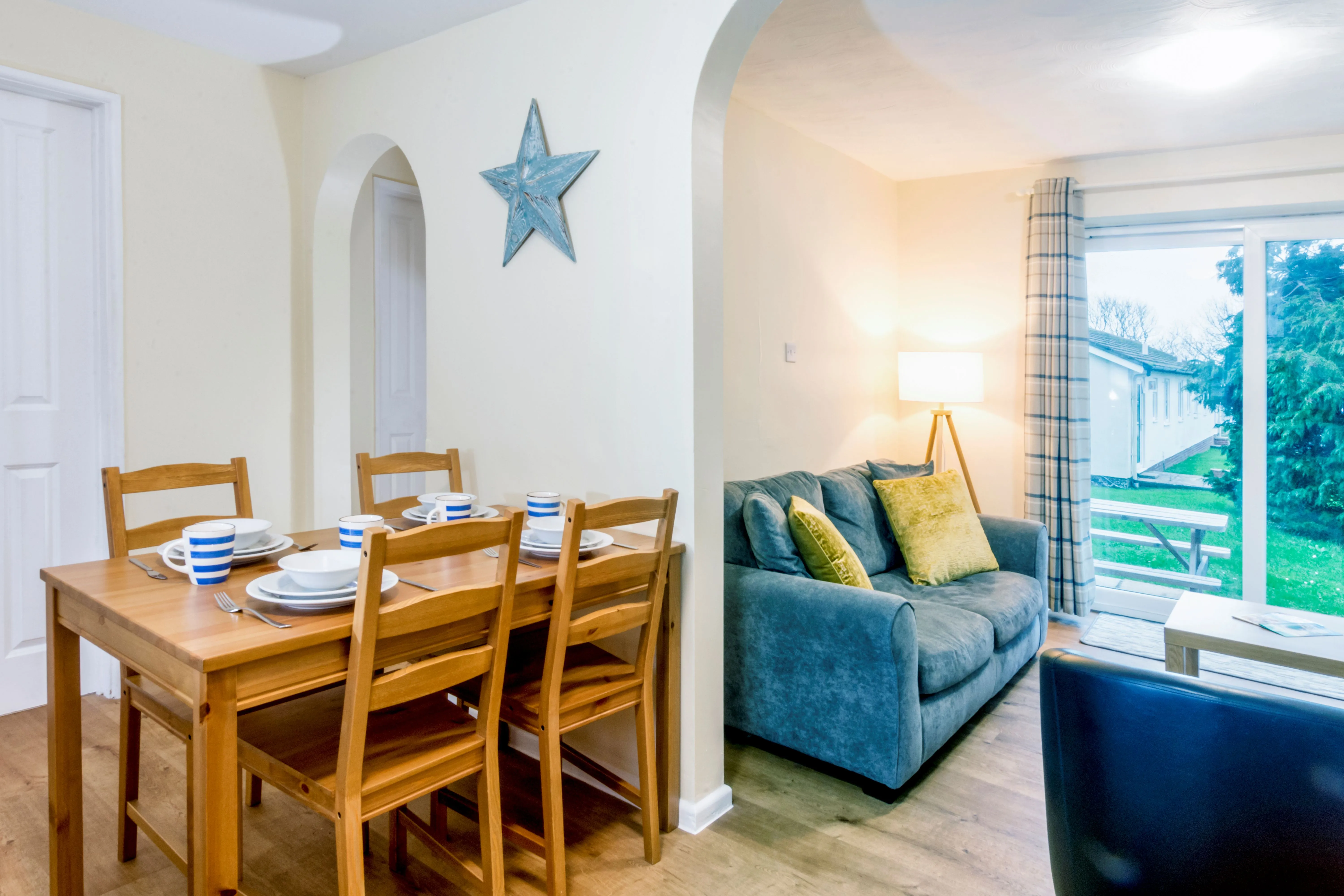 Open-plan dining and lounge area with wooden table, blue sofa and patio doors