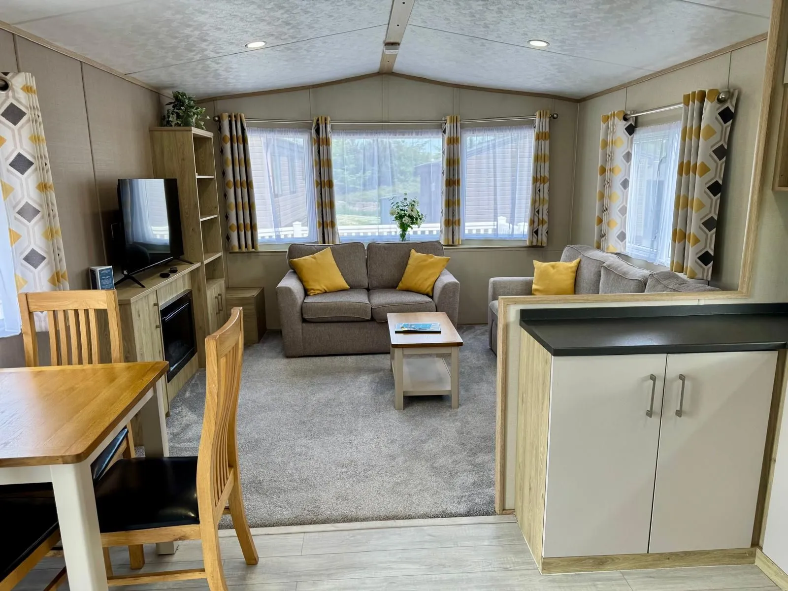 Modern caravan lounge and dining area with grey sofas, yellow cushions, large windows and a TV unit