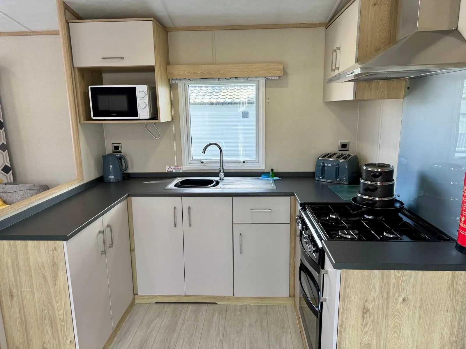 Modern static caravan kitchen with wood-effect units, sink, microwave, kettle, toaster and gas cooker