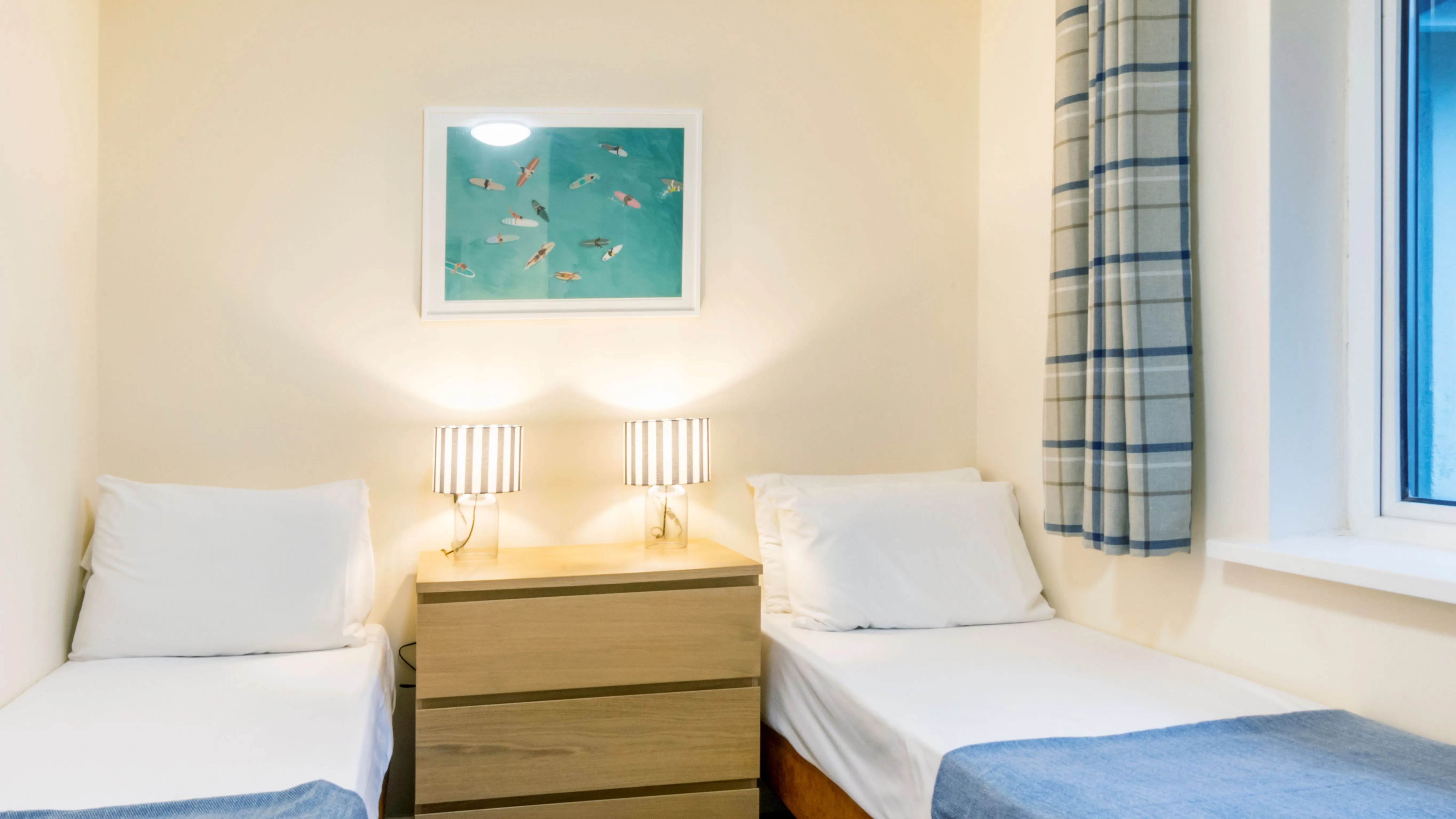 Twin bedroom with two single beds, blue throws, bedside chest of drawers and striped lamps