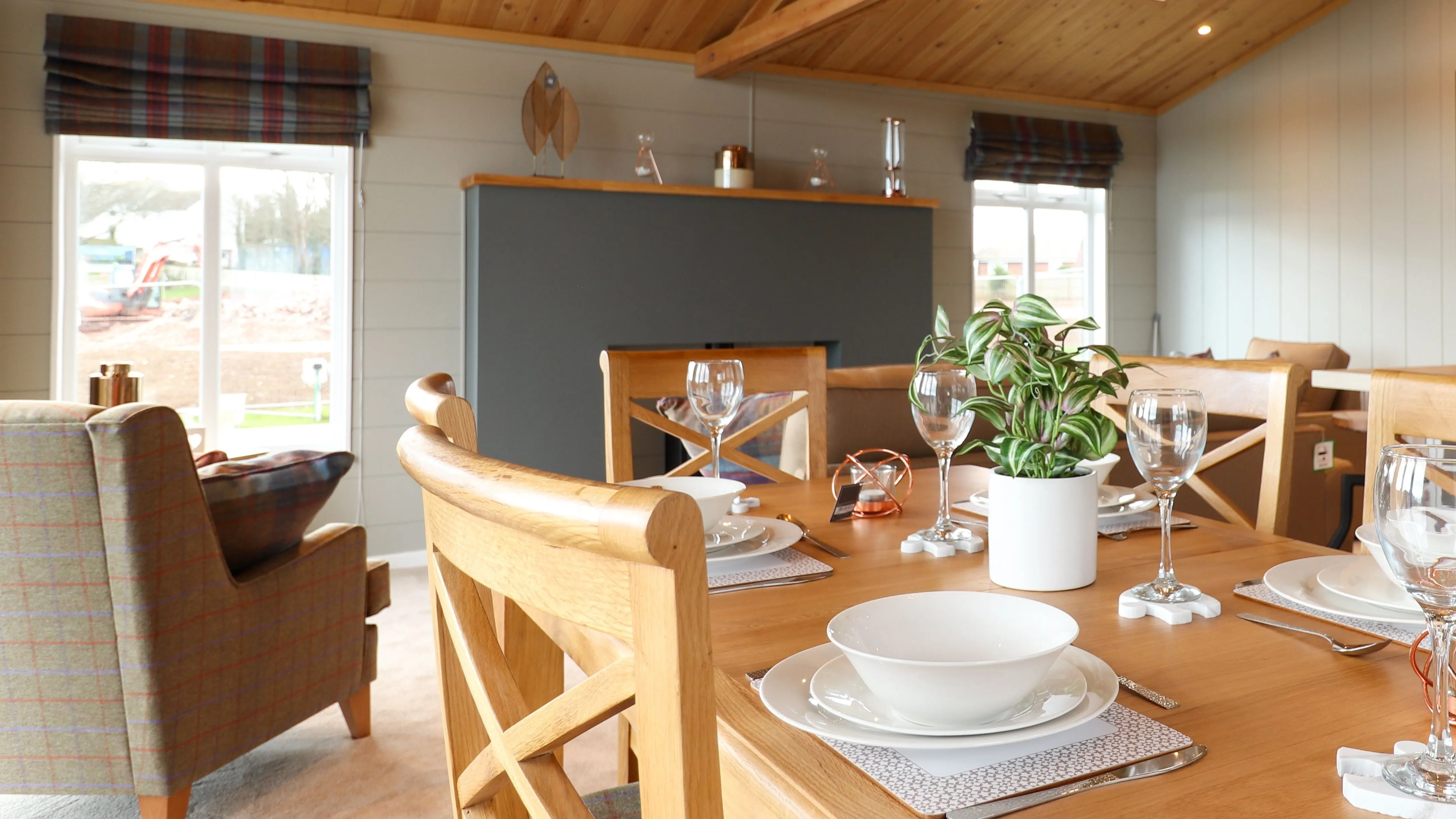 Open-plan lodge interior with wooden vaulted ceiling, dining table, kitchen island and cosy seating area