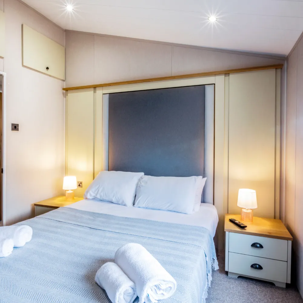 Cosy double bedroom with blue headboard, bedside lamps and folded towels