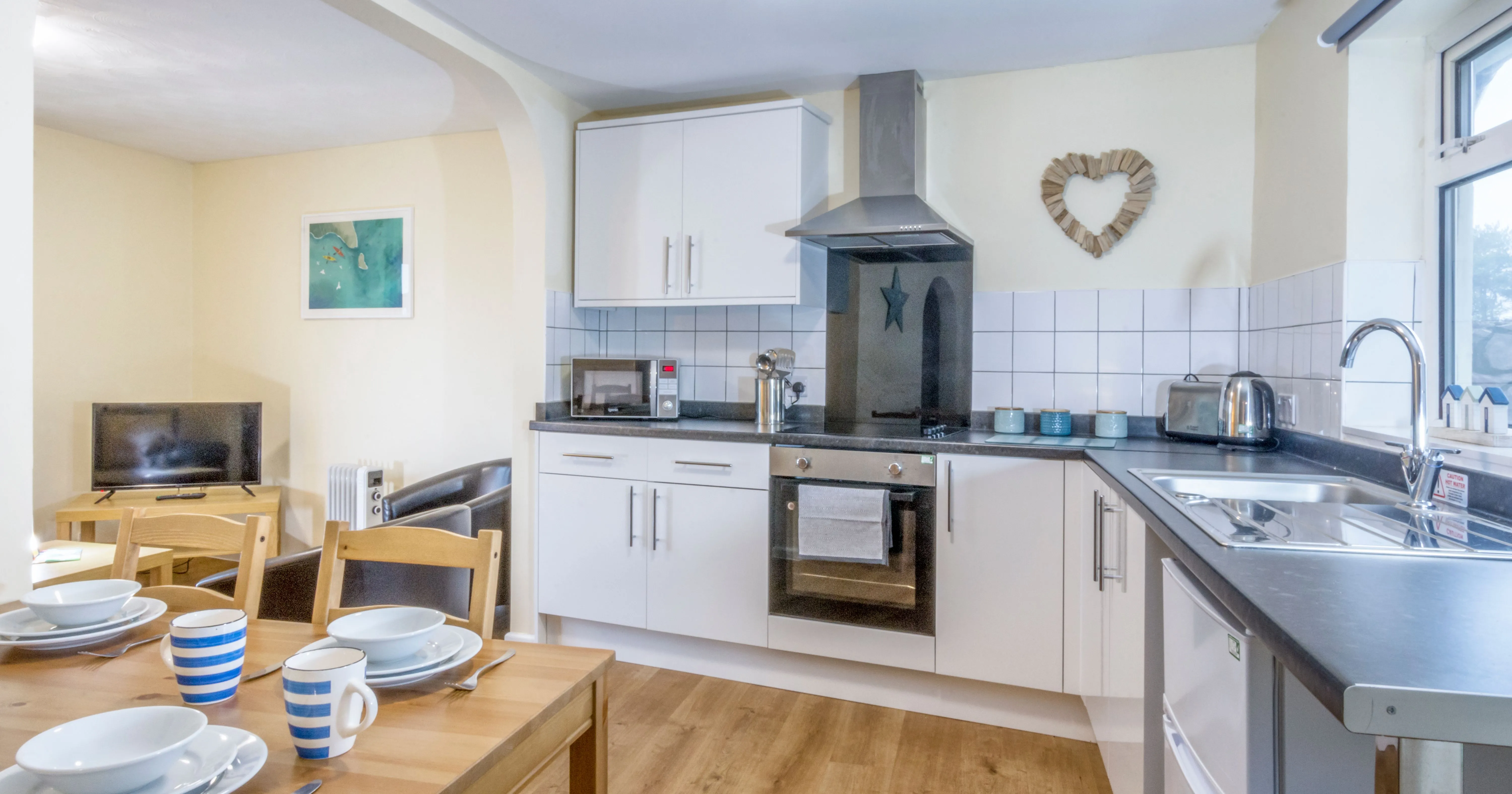 Bright open-plan kitchen and dining area with white units, wooden table and small lounge space
