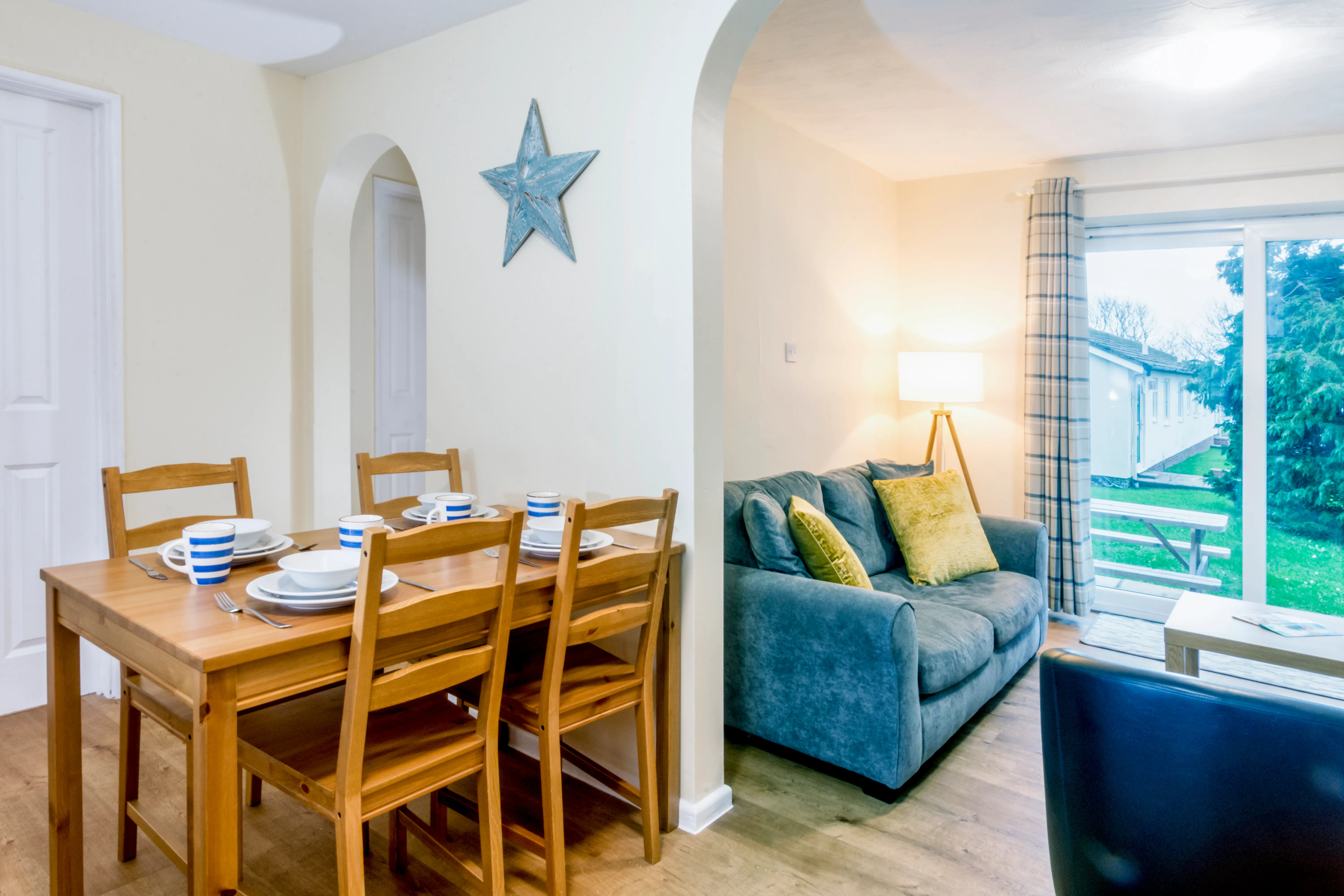 Open-plan dining and living area with wooden dining table, grey sofa and patio doors