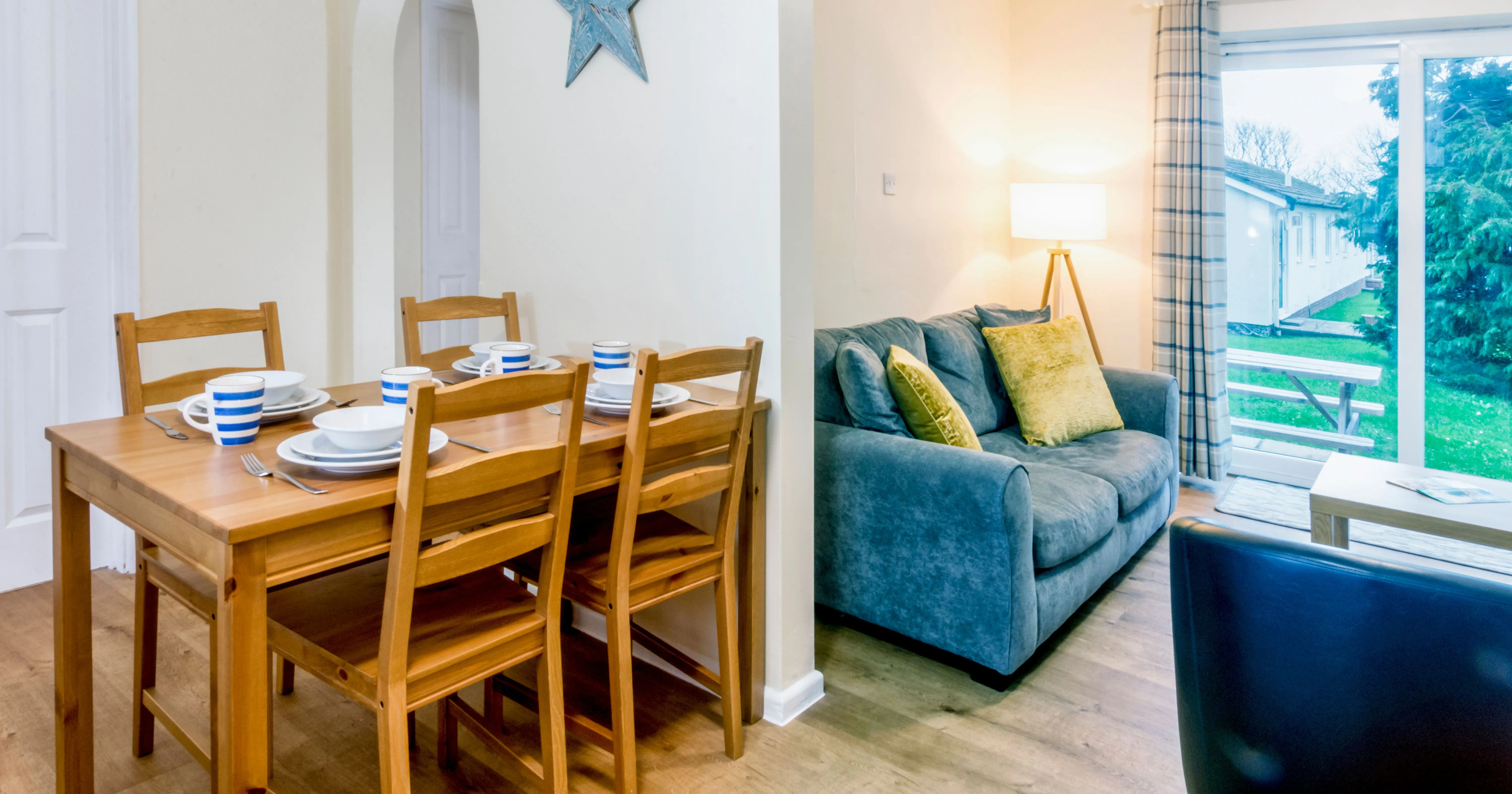 Open-plan dining and living area with wooden dining table, grey sofa and patio doors
