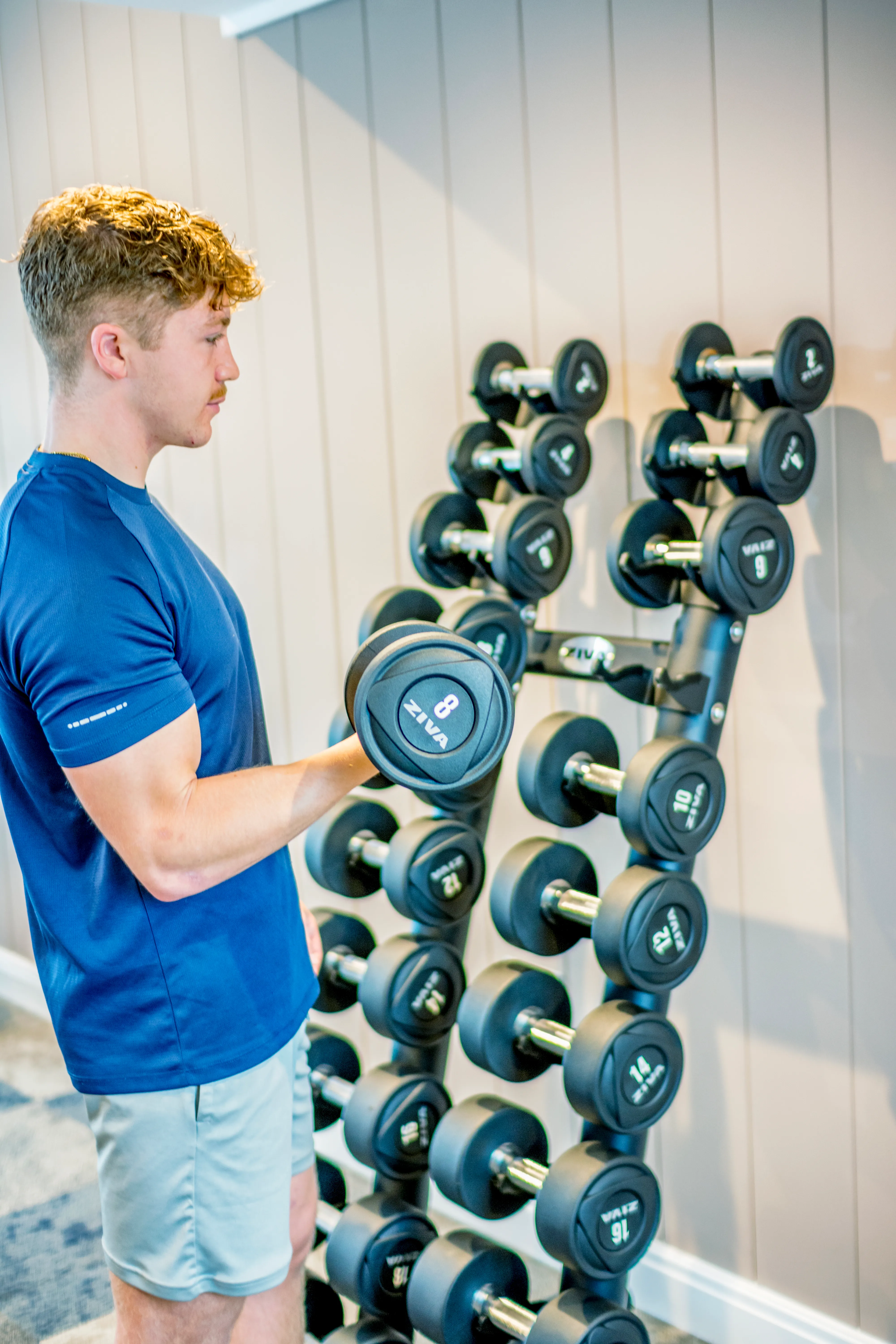 Young man performing a dumbbell bicep curl beside a weight rack in a gym