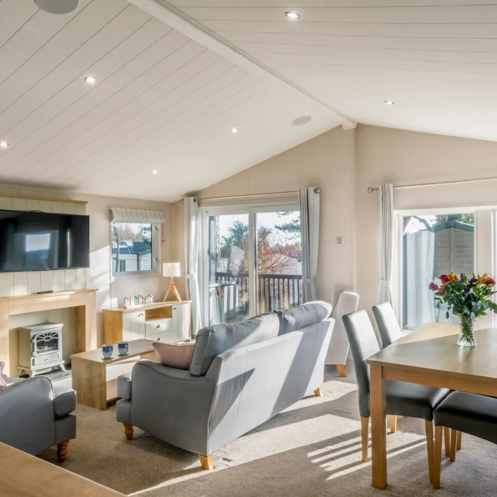 Bright lodge lounge with grey sofas, dining table, wall-mounted TV and sliding doors to a balcony