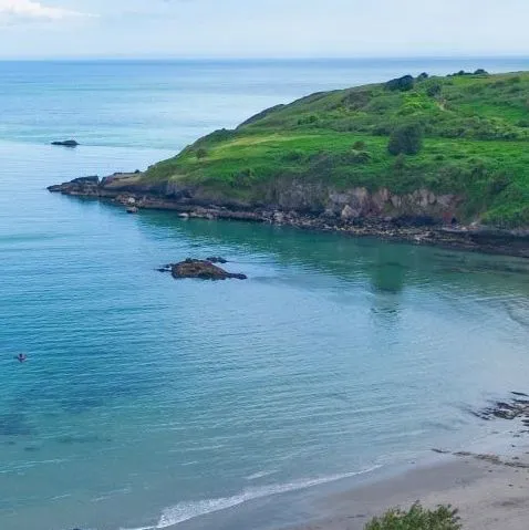 Drone view of Riviera Bay with holiday lodges overlooking a sandy beach, calm turquoise water and a green headland.