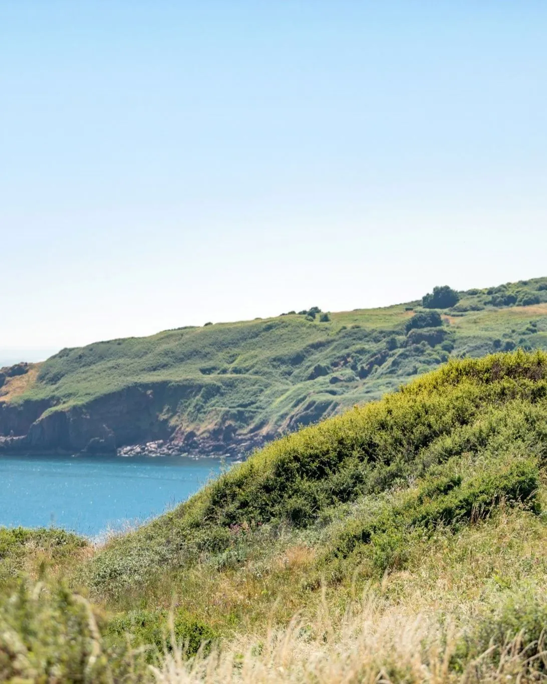 Walker on a coastal path overlooking a calm bay and green cliffs near Landscove Holiday Park