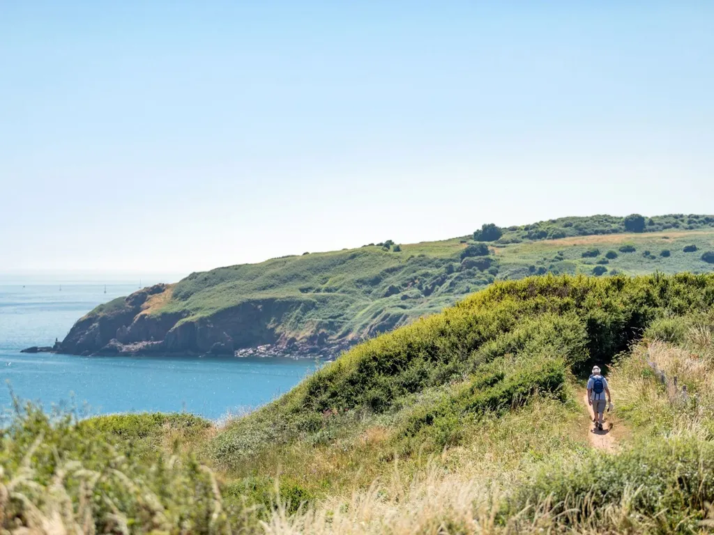 Walker on a coastal path overlooking a calm bay and green cliffs near Landscove Holiday Park