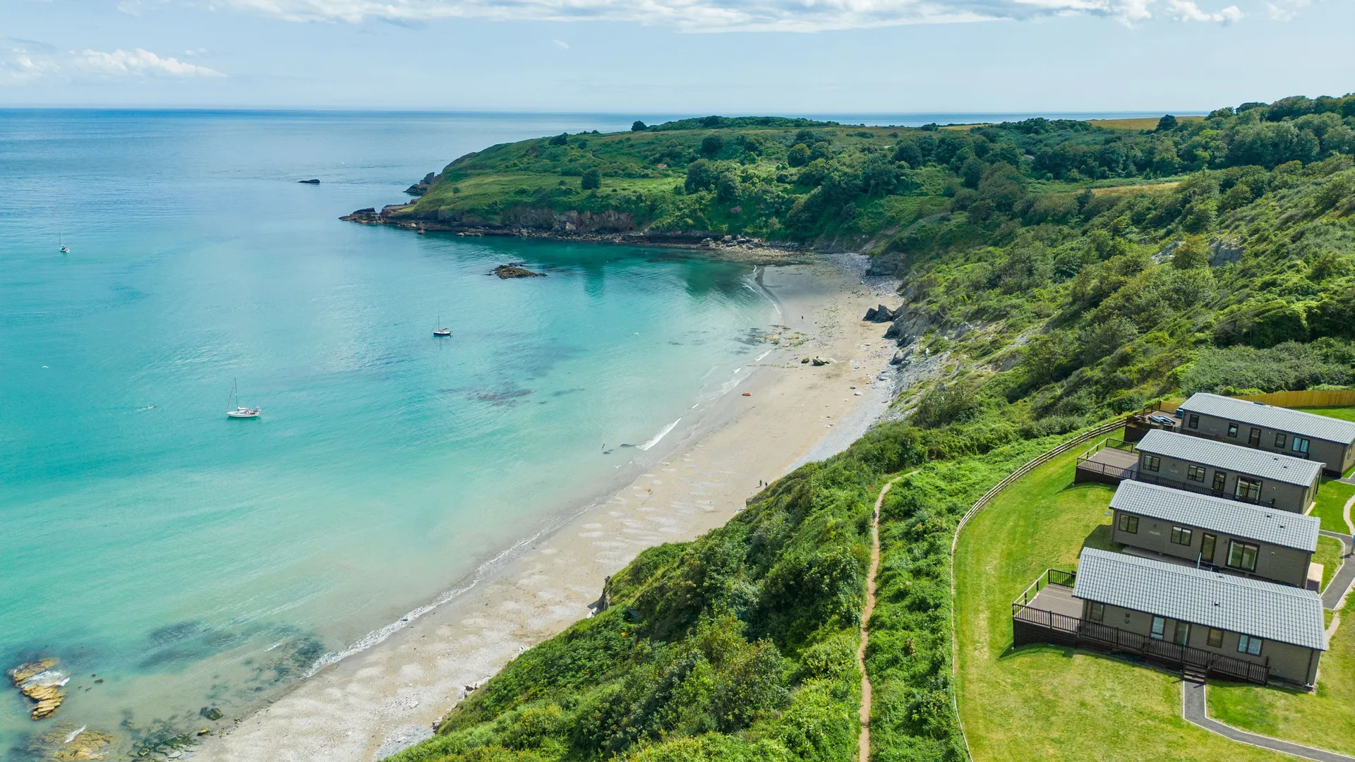Drone view of Riviera Bay with a sandy beach, turquoise sea and holiday lodges on the clifftop