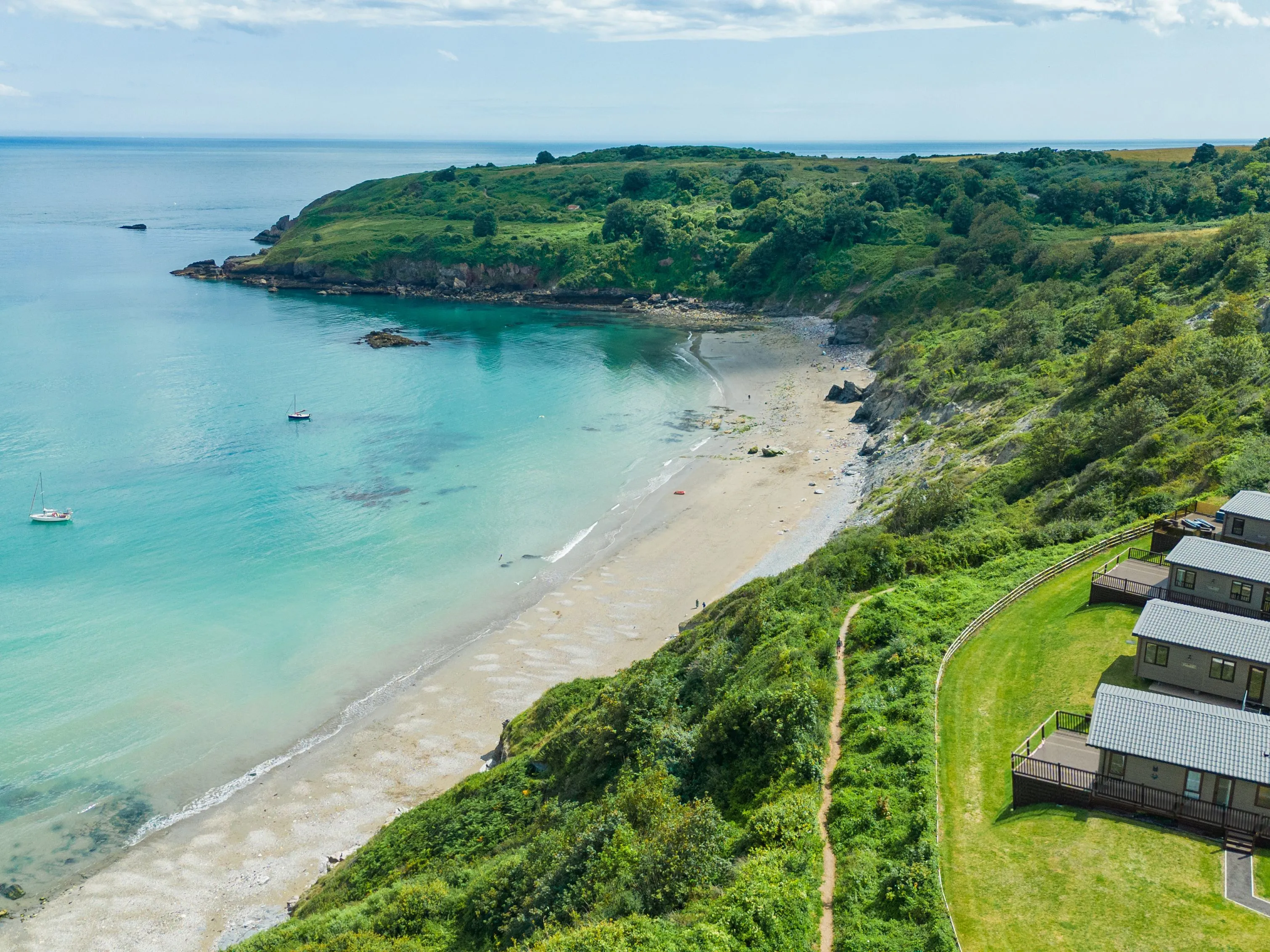 Drone view of Riviera Bay with a sandy beach, turquoise sea and holiday lodges on the clifftop