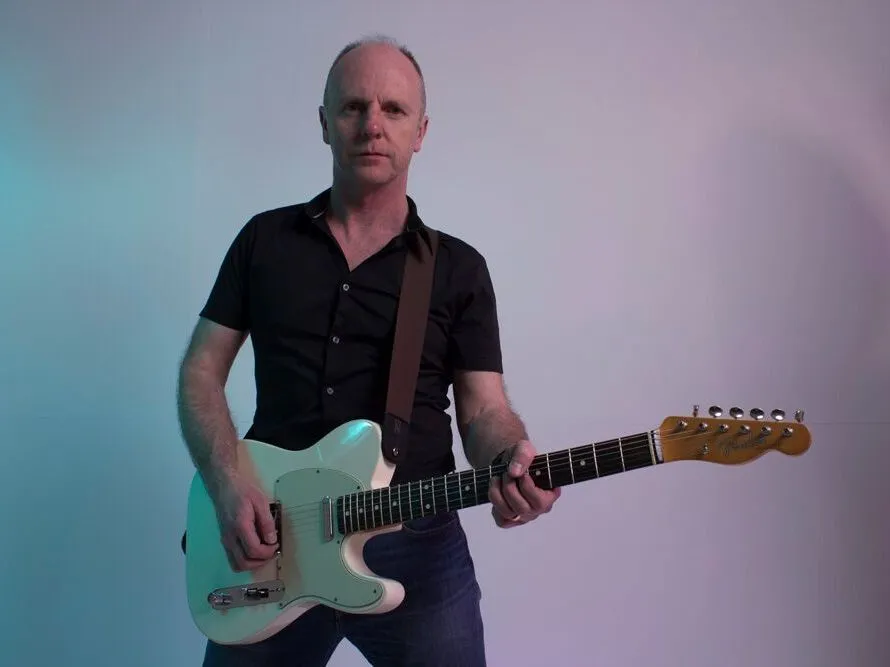 Man holding a white electric guitar against a softly lit studio background