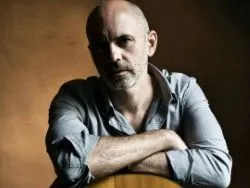 Portrait of a bald bearded man leaning on an acoustic guitar against a dark background
