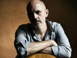 Portrait of a bald bearded man leaning on an acoustic guitar against a dark background