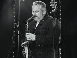Black and white photo of a saxophonist performing on stage beside a microphone.