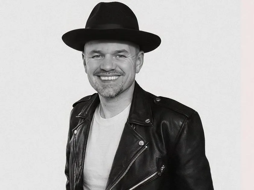 Black-and-white portrait of a smiling man wearing a black hat and leather jacket
