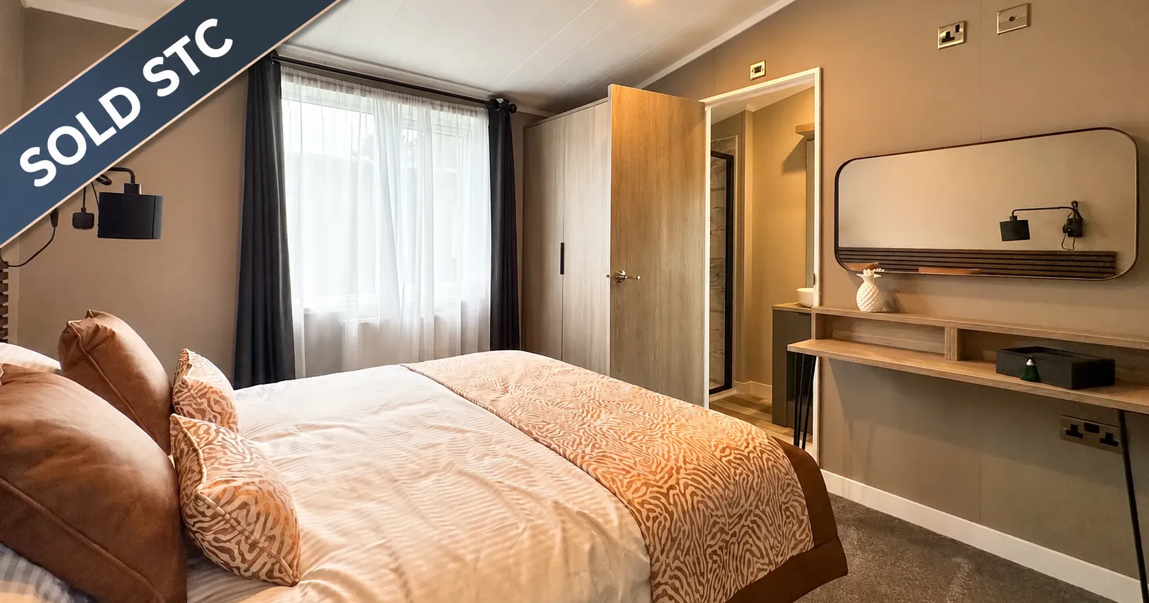 Modern double bedroom with upholstered bed, feature cushions, large window, fitted wardrobe and dressing table with mirror, marked Sold STC.