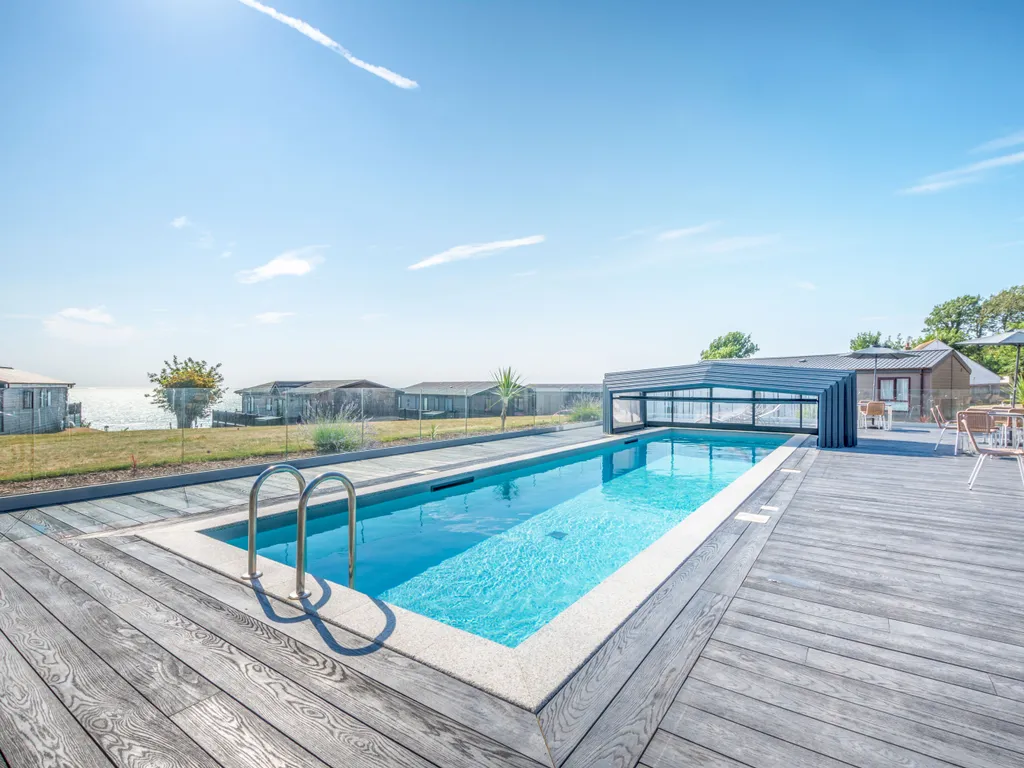 Outdoor swimming pool with a timber deck, retractable cover and sea view beside holiday lodges.