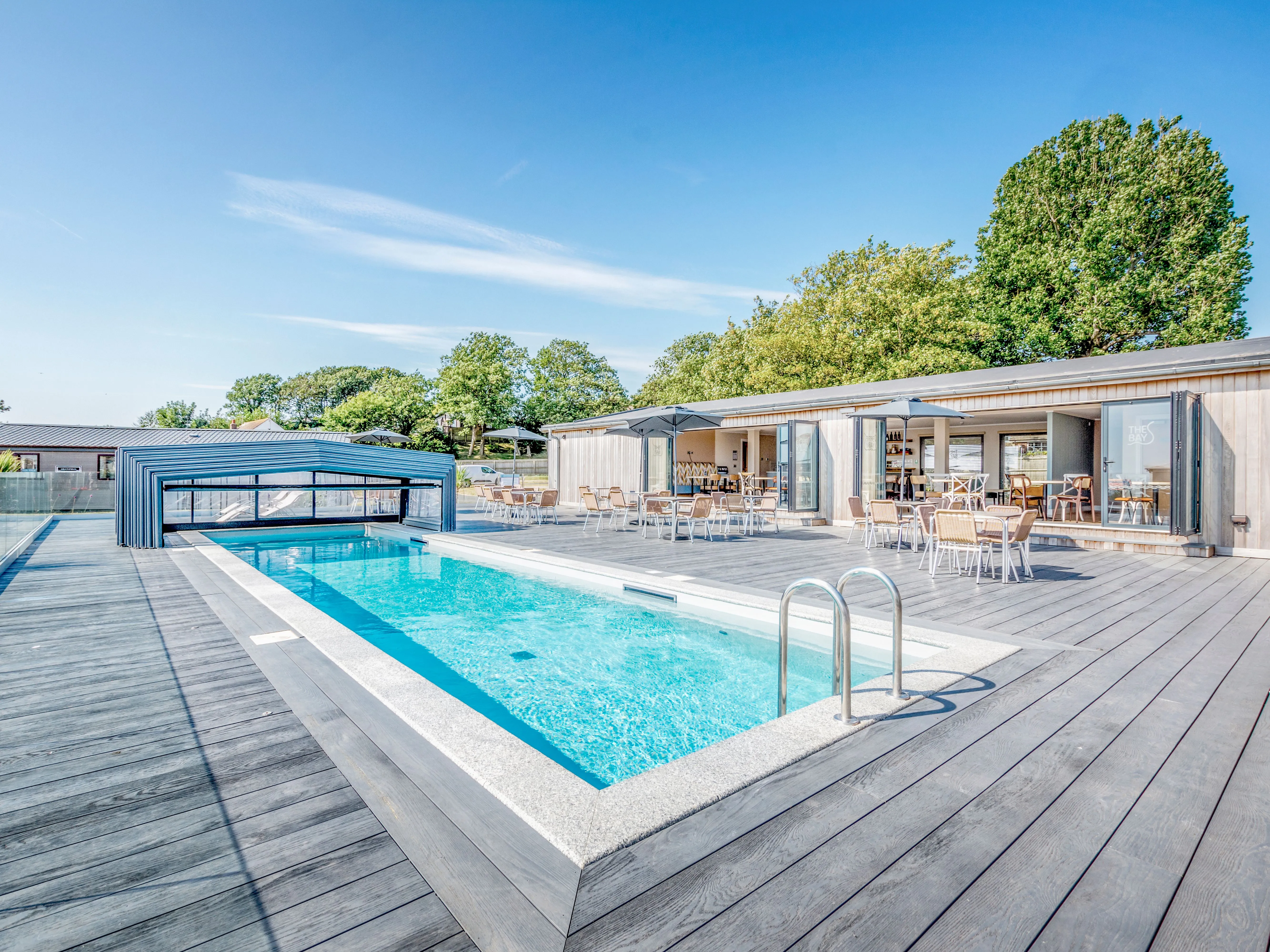Outdoor swimming pool with a modern slatted canopy, timber decking and café terrace seating.