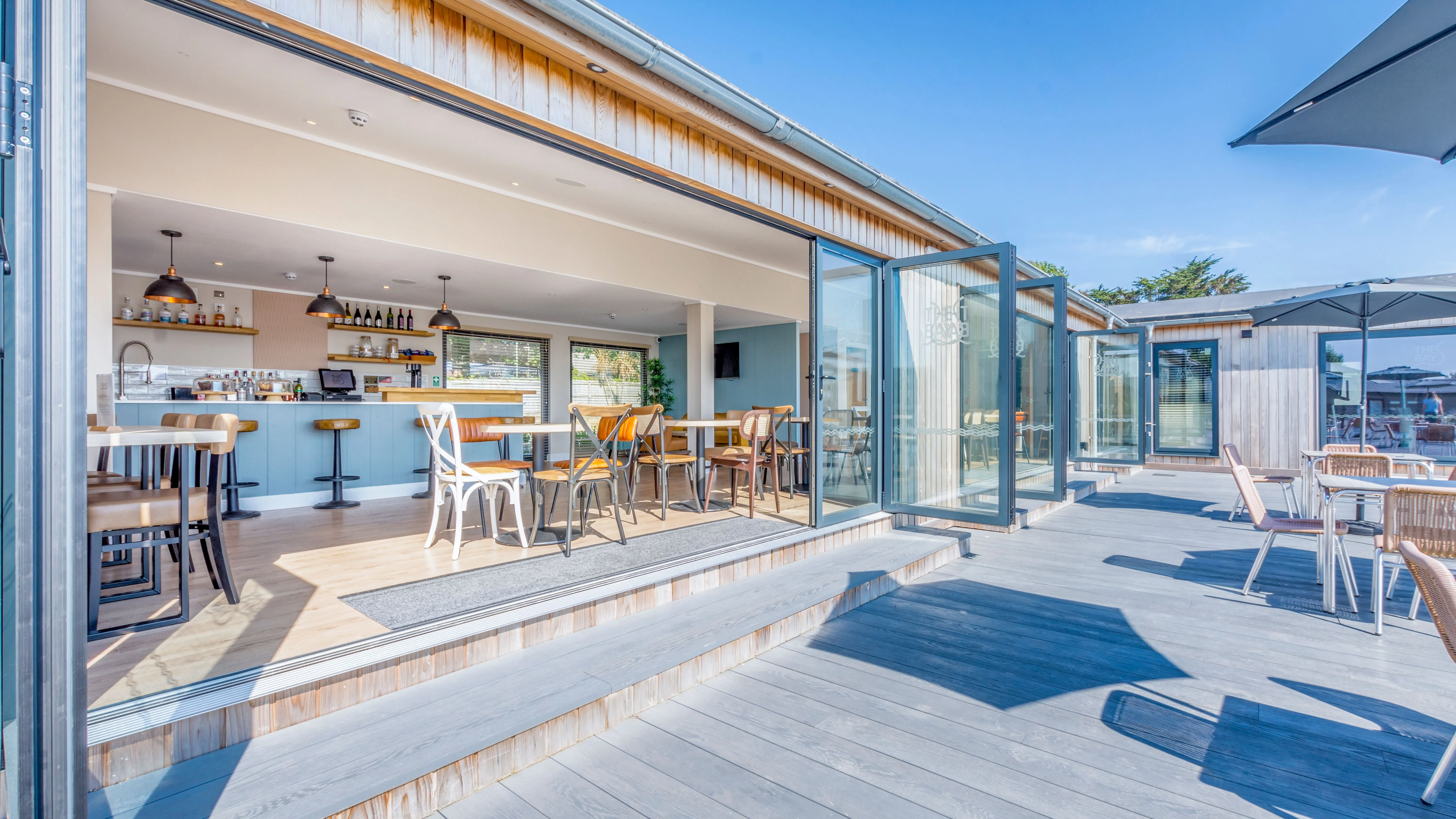 Open-plan café bar with folding glass doors leading to a sunny outdoor terrace.