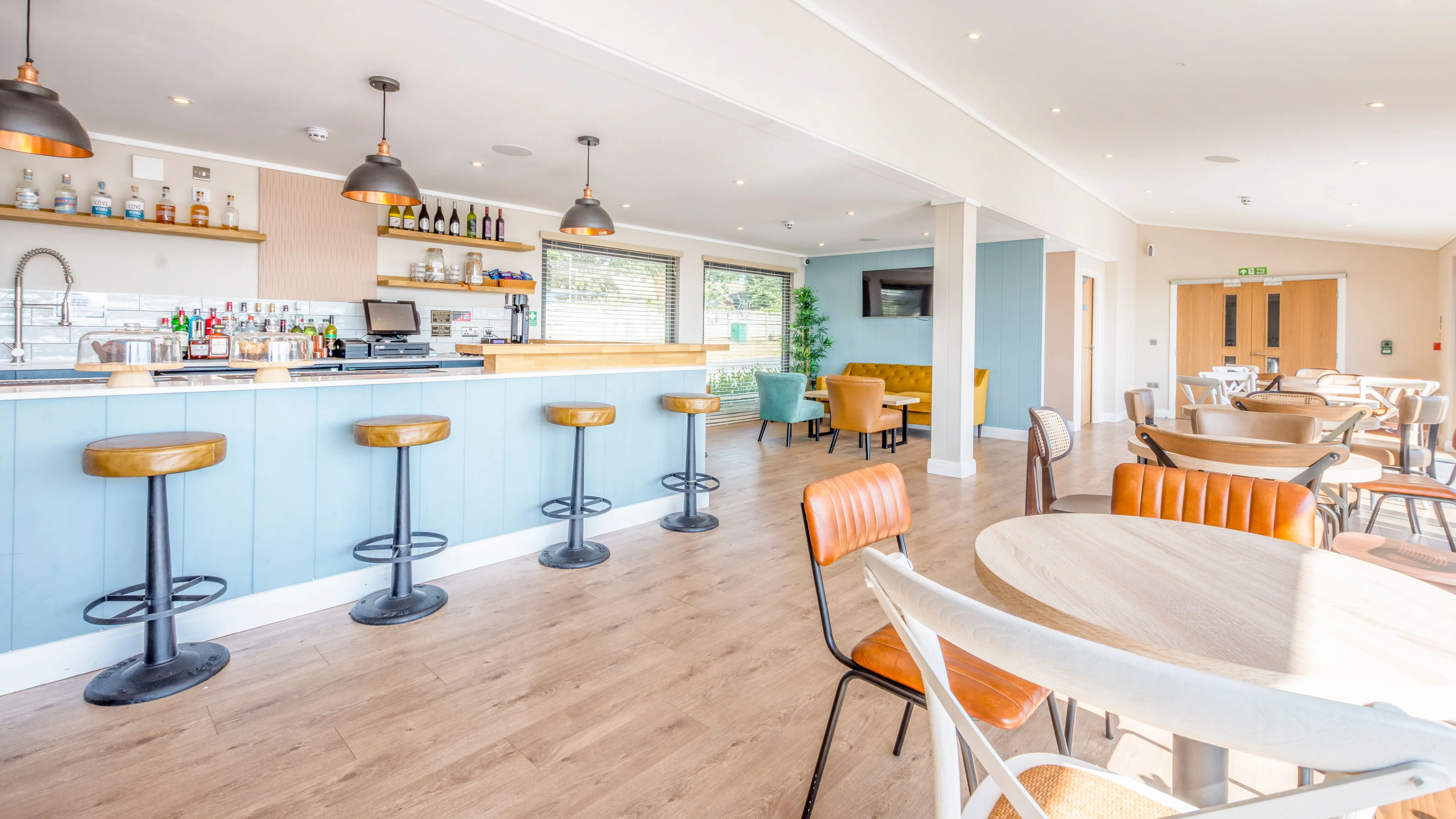 Bright modern café bar with pale blue counter, leather stools and dining tables