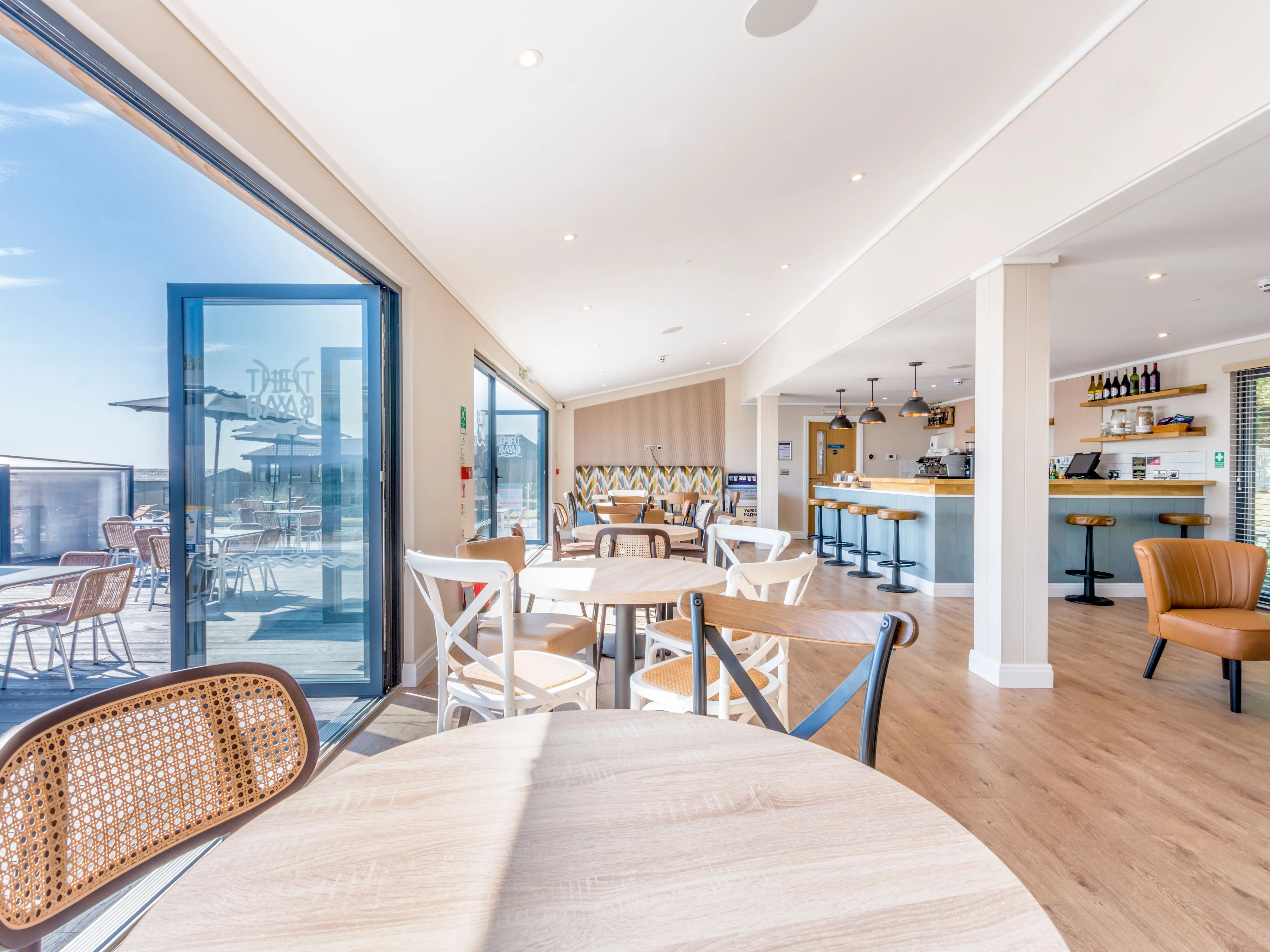 Bright modern café interior with wooden tables, bar seating and open doors to an outdoor terrace