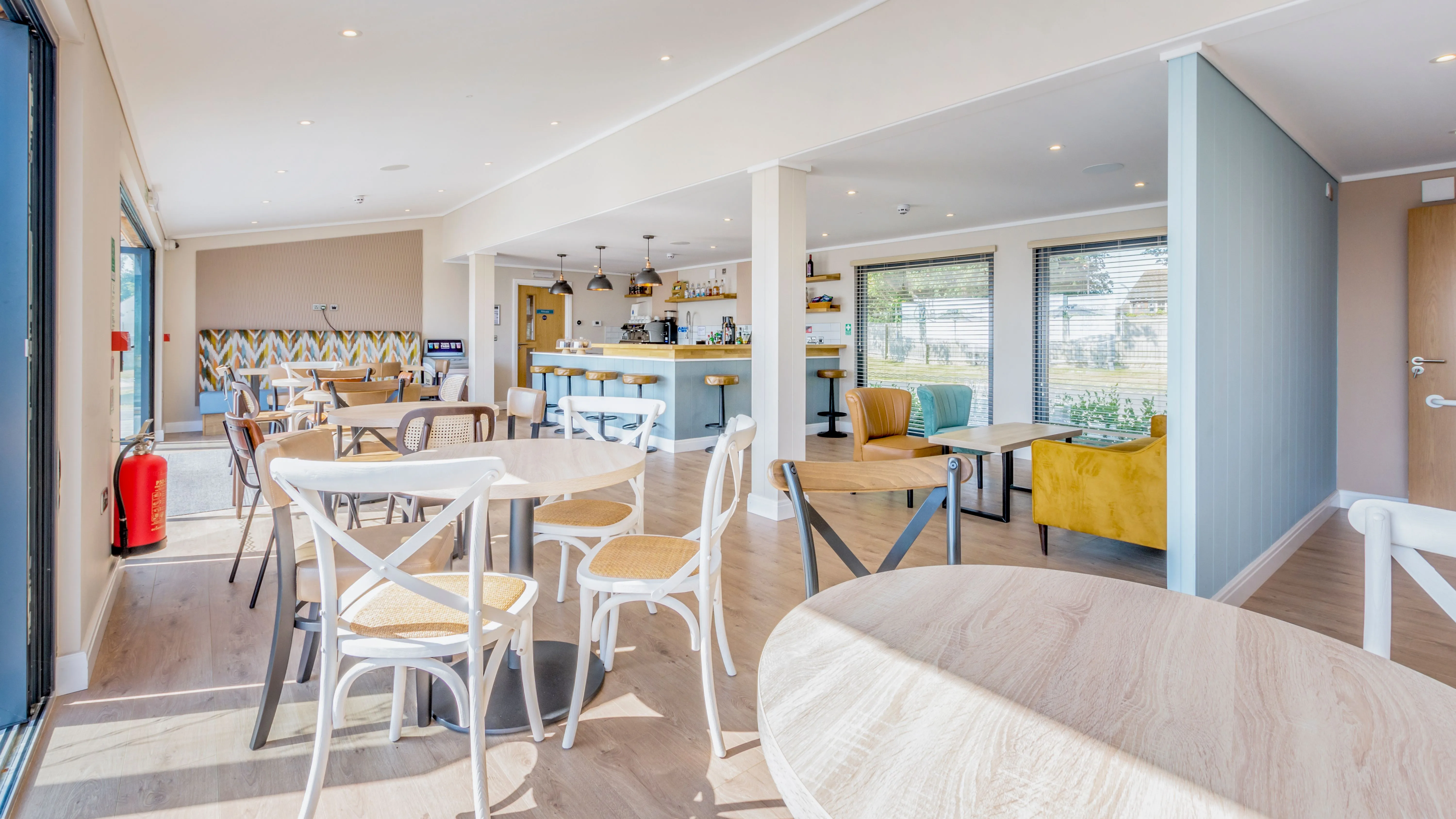Bright modern café lounge with wooden tables, mixed chairs, colourful armchairs and a bar counter.