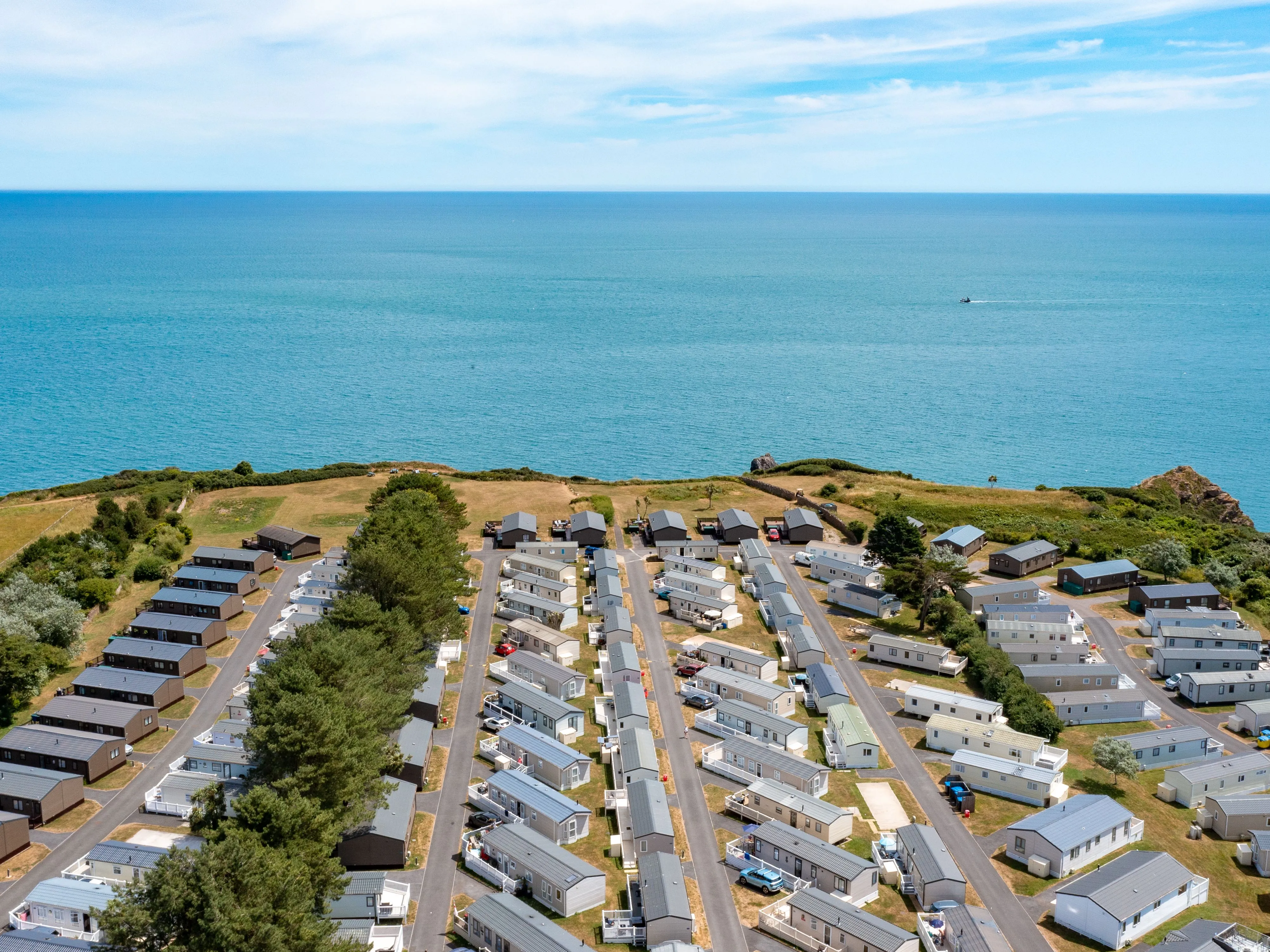 Aerial view of a coastal holiday park with static caravans beside a calm blue sea.