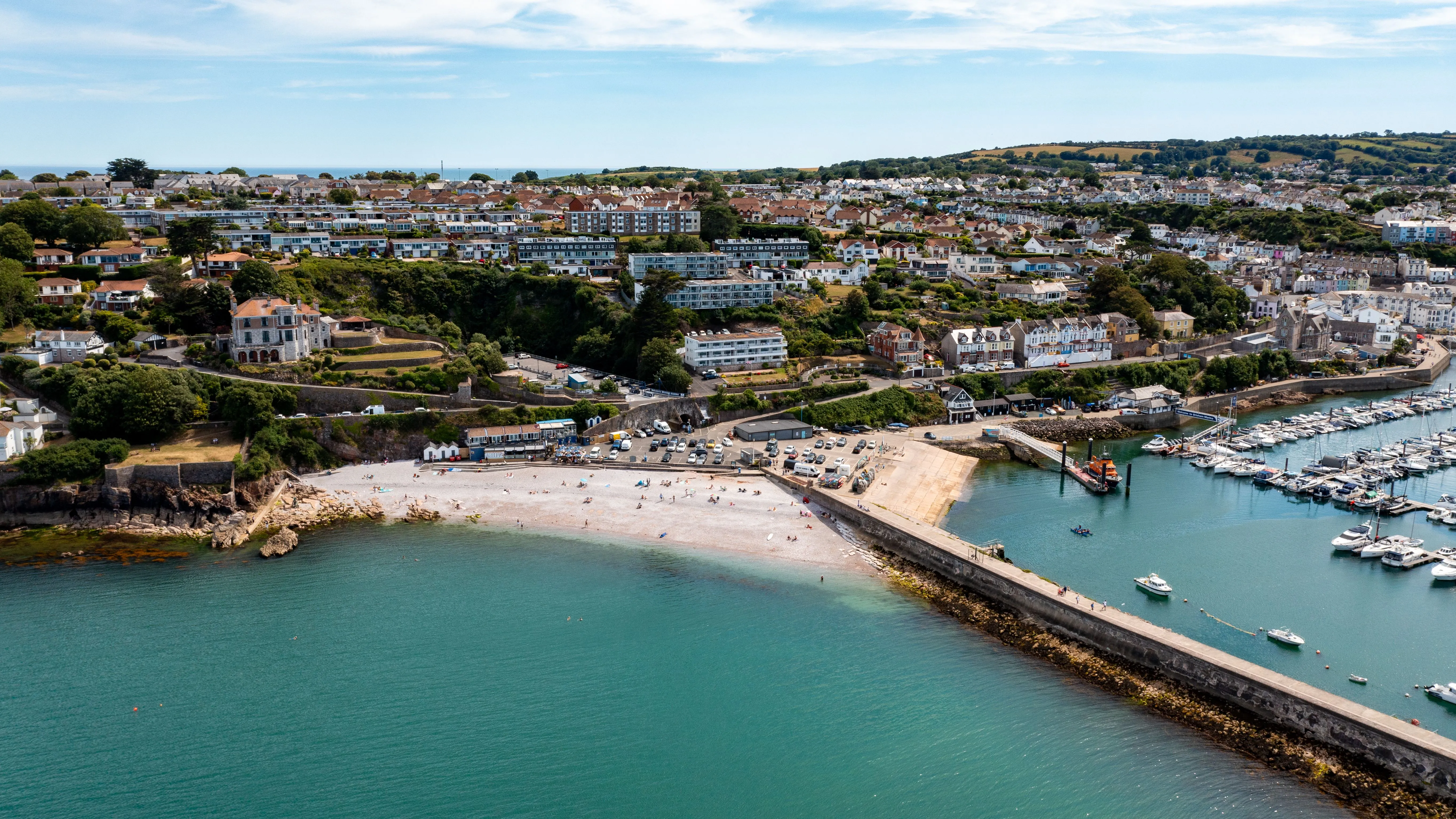 Aerial view of a coastal town with a sandy beach, harbour marina and stone breakwater.