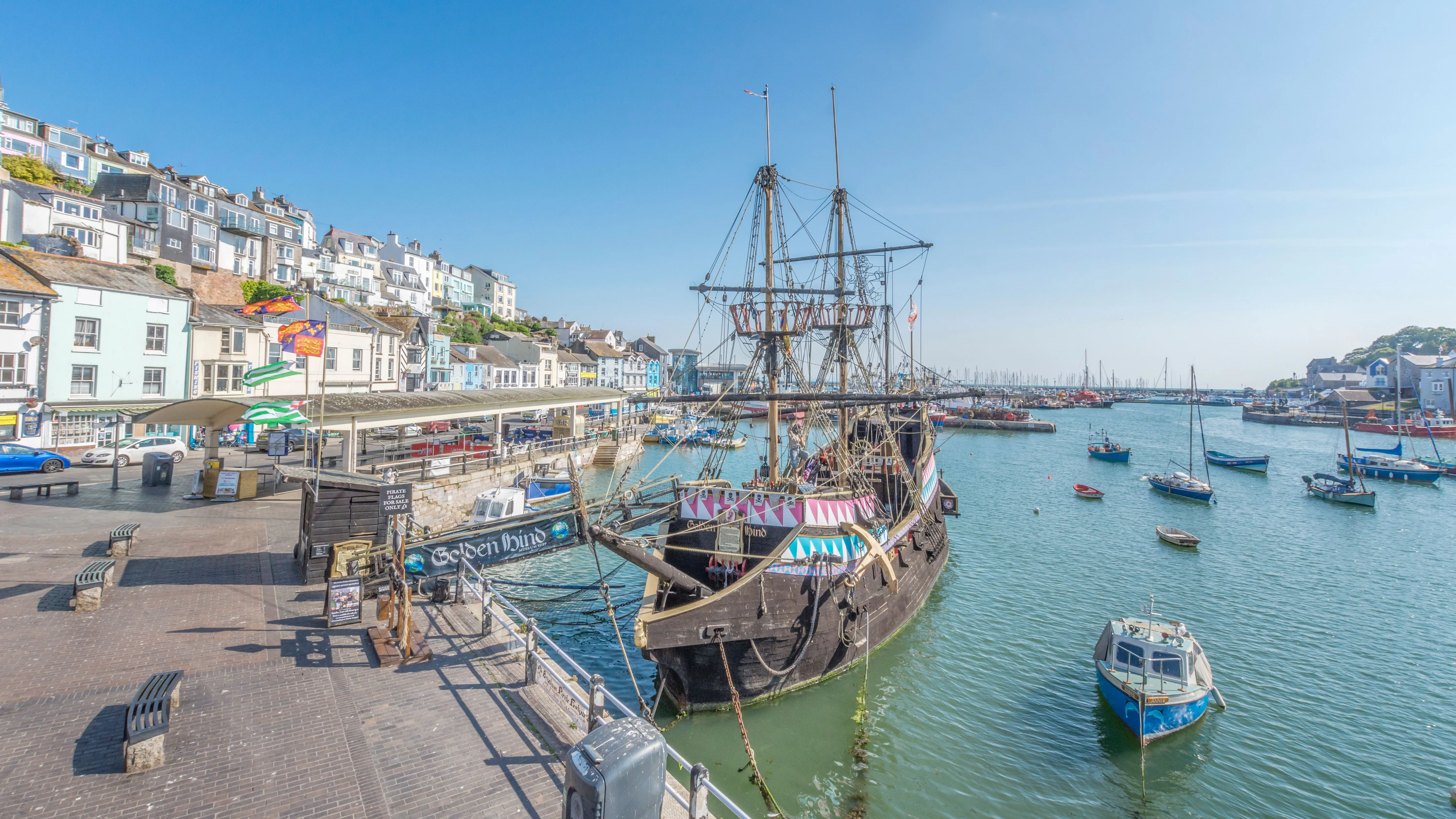 Historic sailing ship moored beside colourful waterfront buildings in Brixham Harbour on a sunny day.