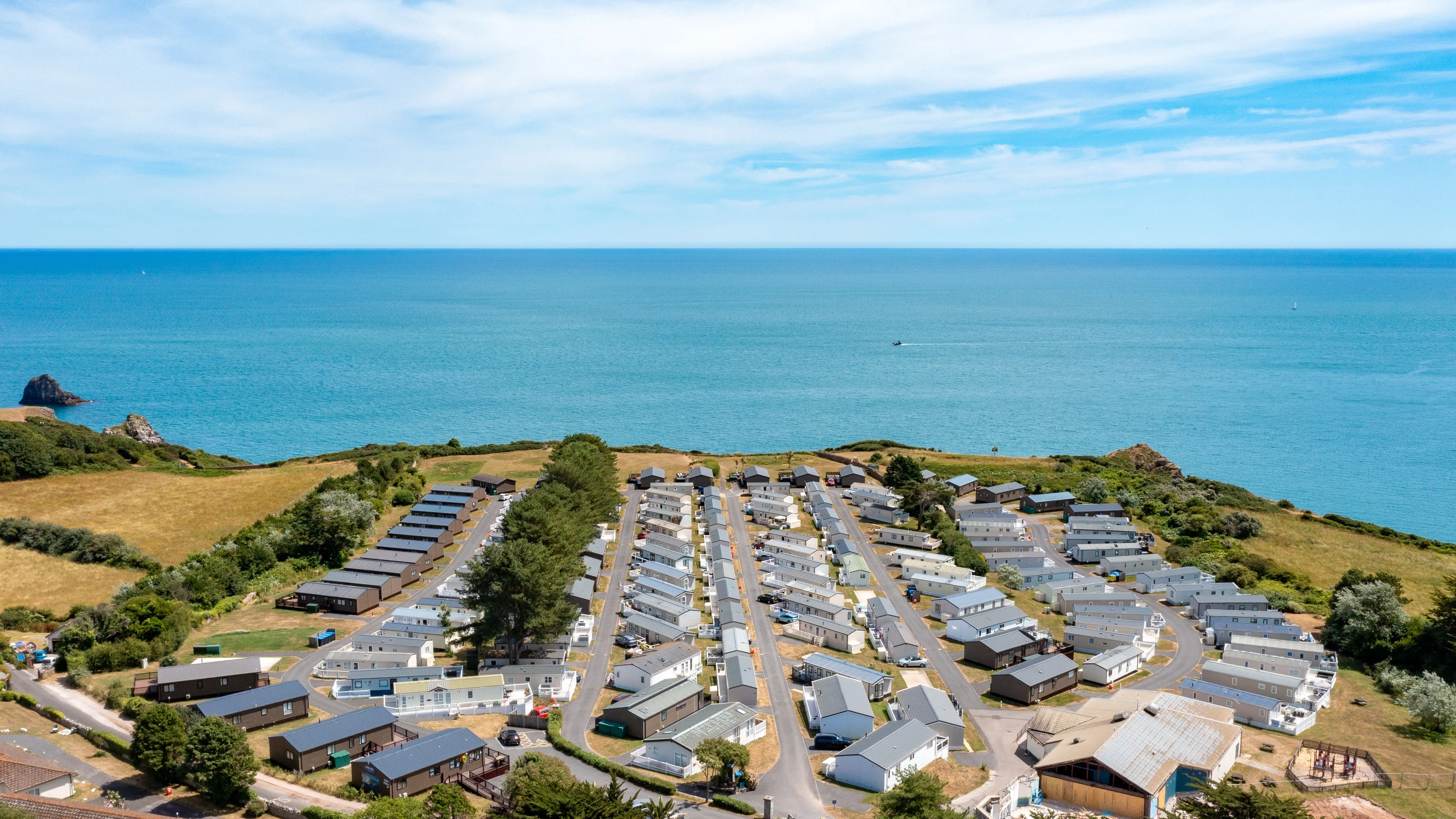 Aerial view of a coastal holiday park with static caravans beside a bright blue sea.