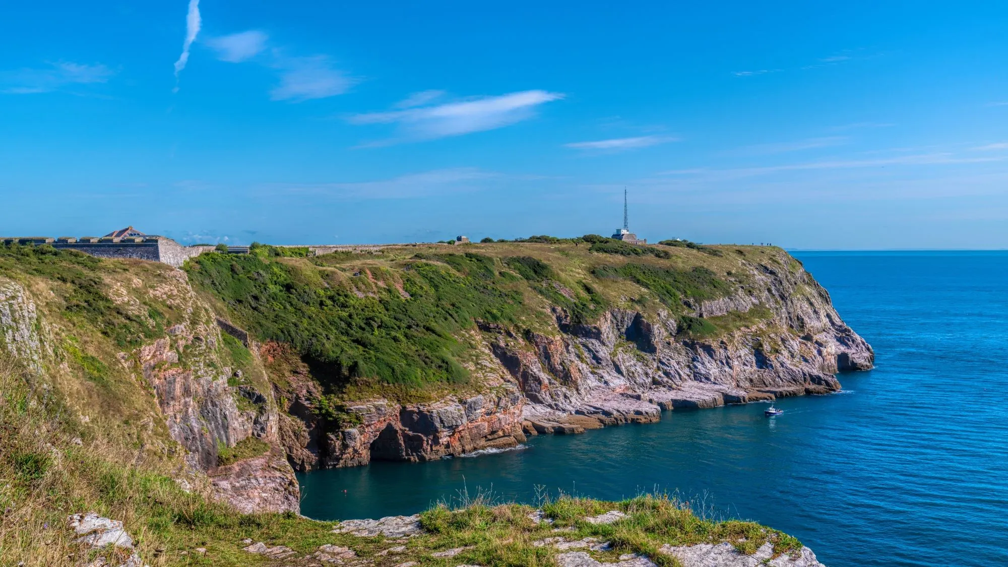 Rocky coastal cliffs with a historic fort and blue sea beneath a clear sky