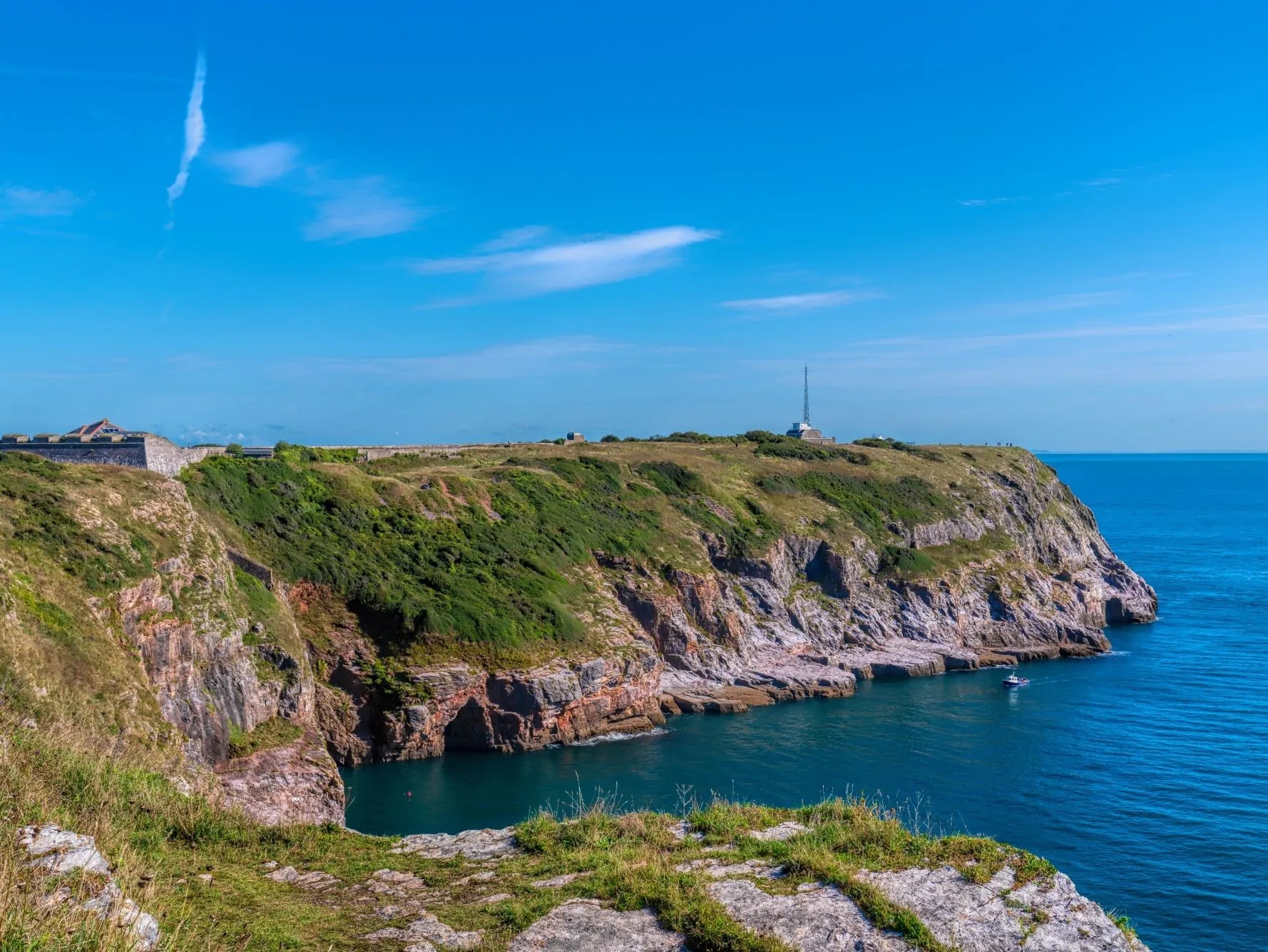 Rocky coastal cliffs with a historic fort and blue sea beneath a clear sky