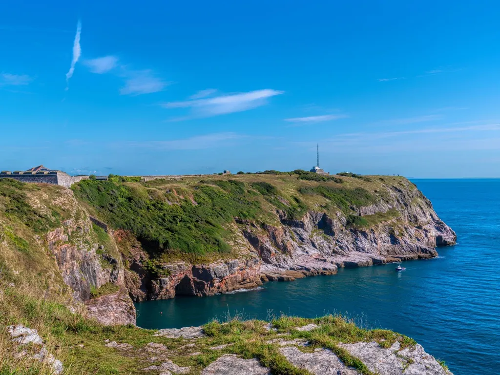 Rocky coastal cliffs with a historic fort and blue sea beneath a clear sky