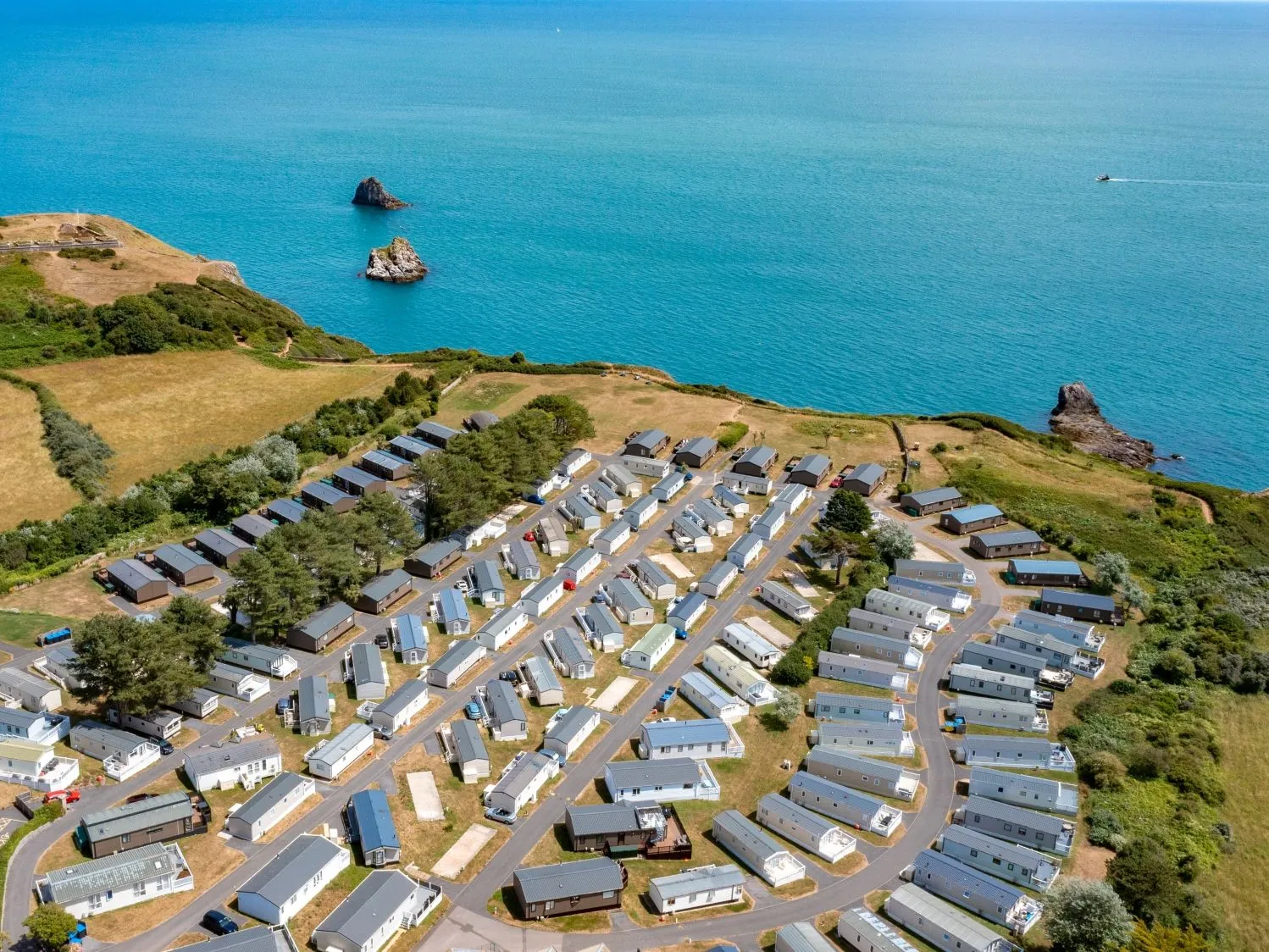 Aerial view of a coastal holiday park with caravans beside turquoise sea and rocky islets.