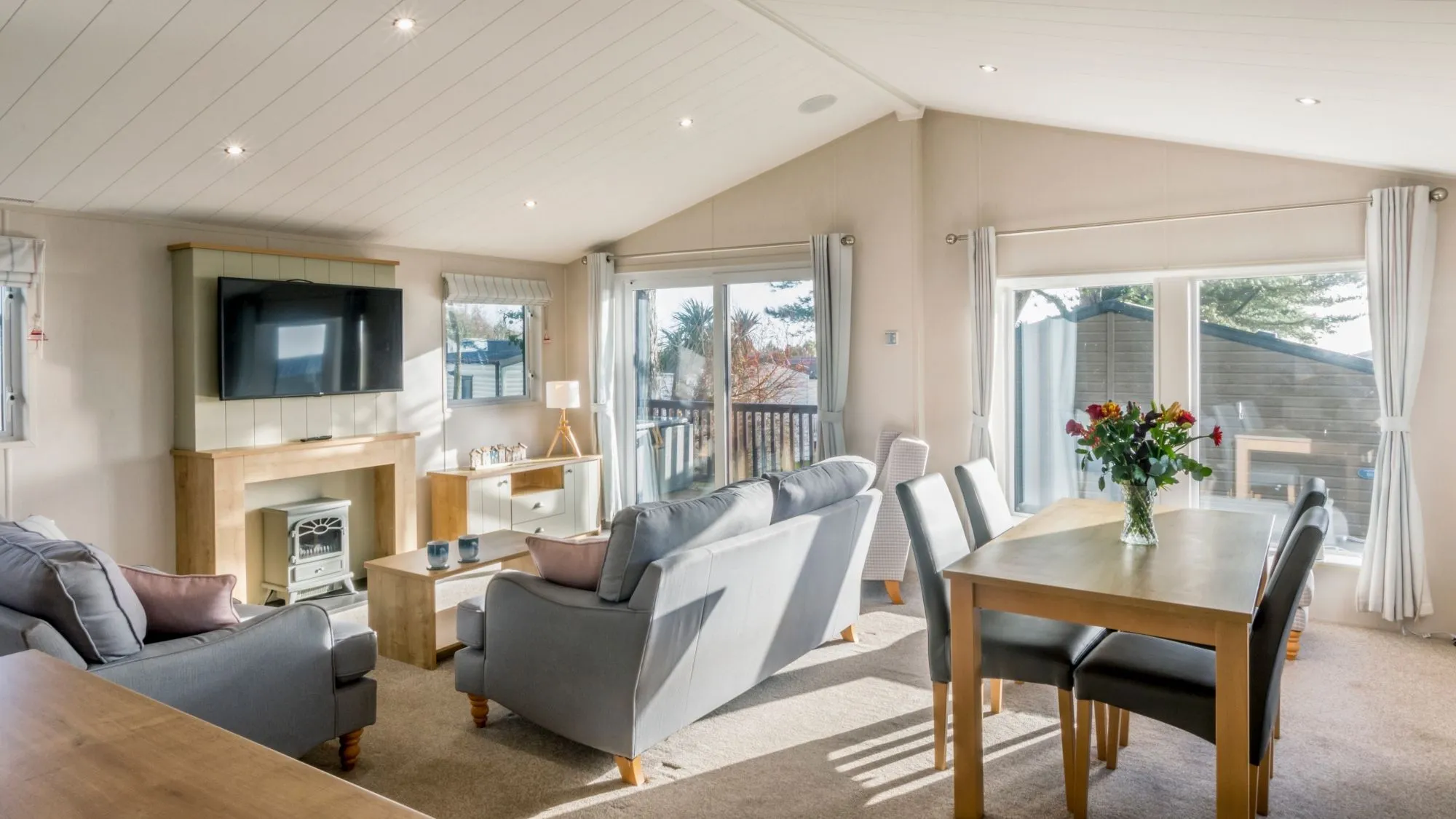 Bright open-plan living and dining room with grey sofas, wooden table and large windows