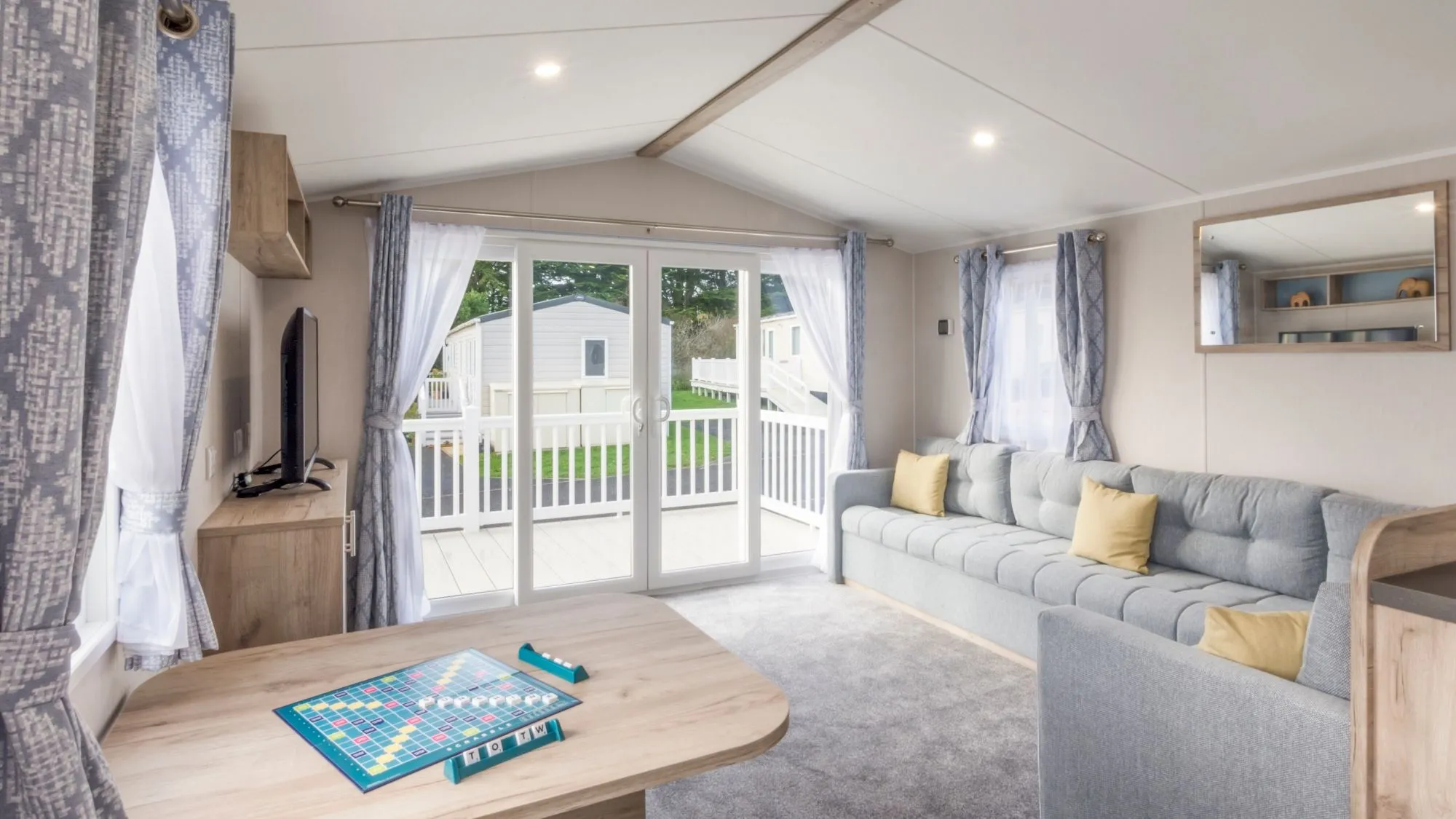 Bright modern holiday lodge living room with grey sofa, television and patio doors