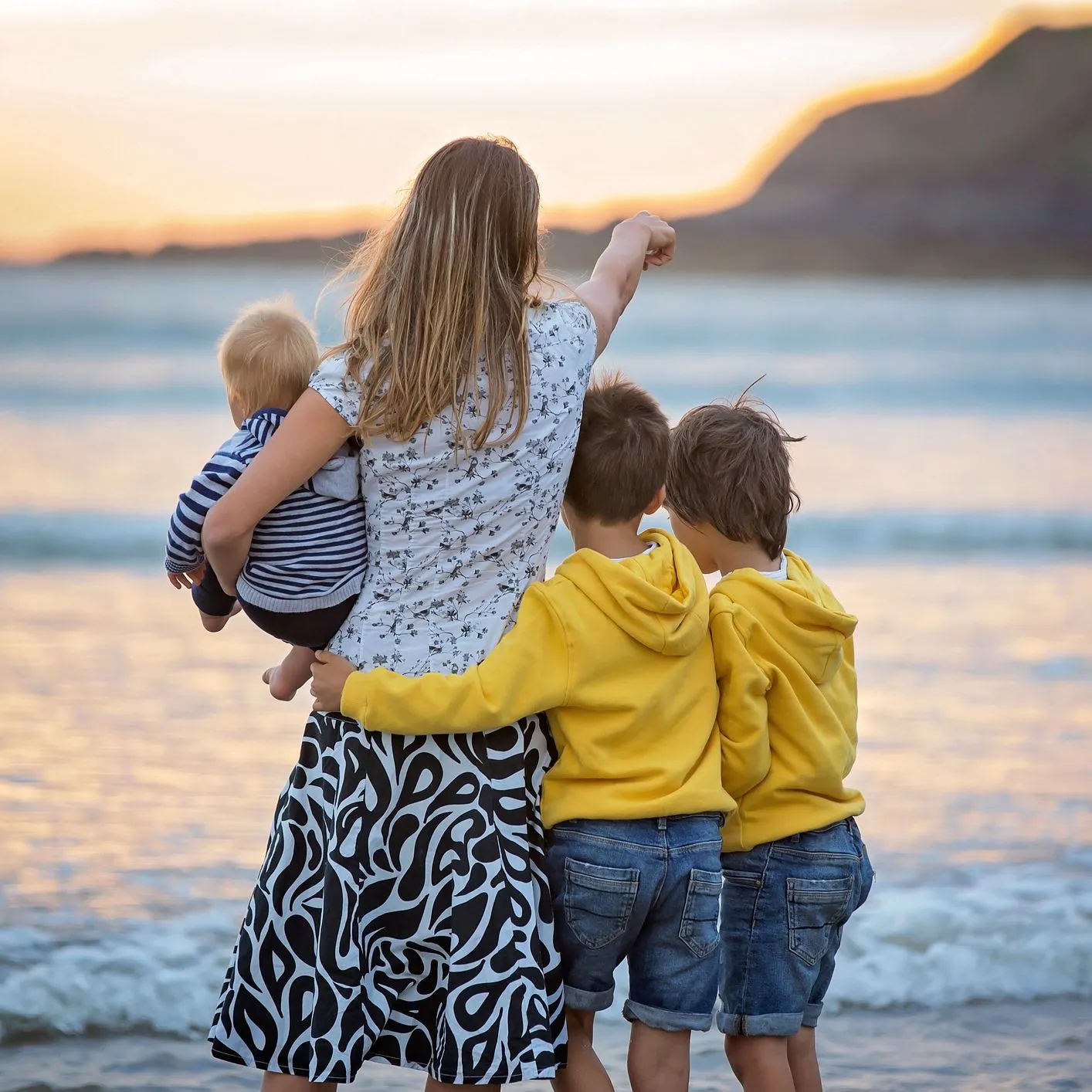 Mother holding a baby with two young boys beside her on a beach at sunset