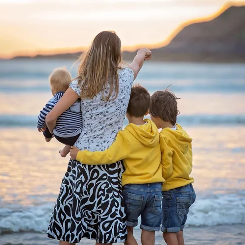 Mother holding a baby with two young boys beside her on a beach at sunset