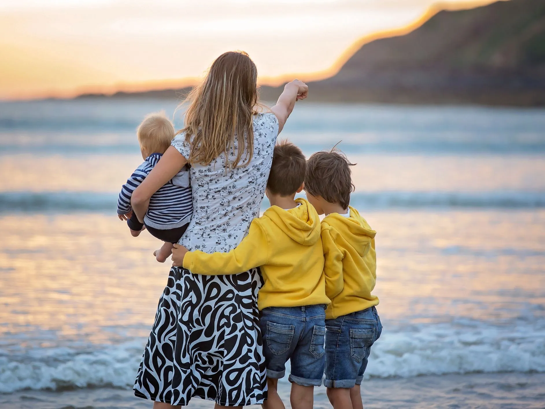 Mother holding a baby with two young boys beside her on a beach at sunset
