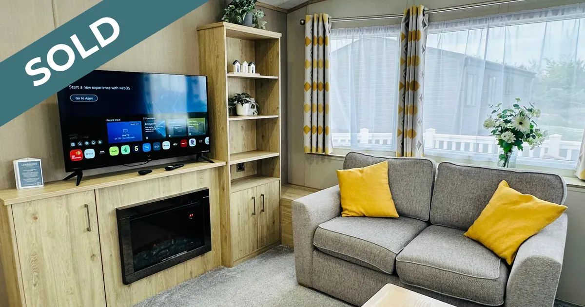 Cosy modern caravan lounge with grey sofa, yellow cushions, television and electric fireplace, marked sold.
