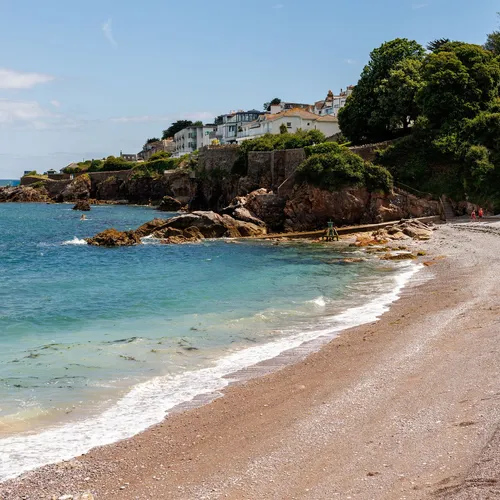 Pebble beach with turquoise sea beneath houses and greenery on a rocky coastal hillside