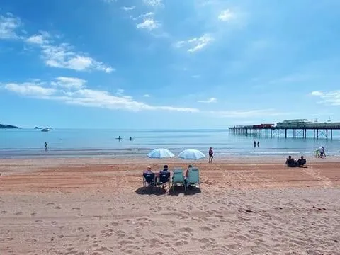 Sunny view of Paignton Sands with people relaxing on the beach, calm sea and a pier extending into the water