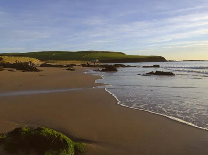 Sandy shoreline with gentle waves and rocky outcrops at Bantham Beach under a clear sky