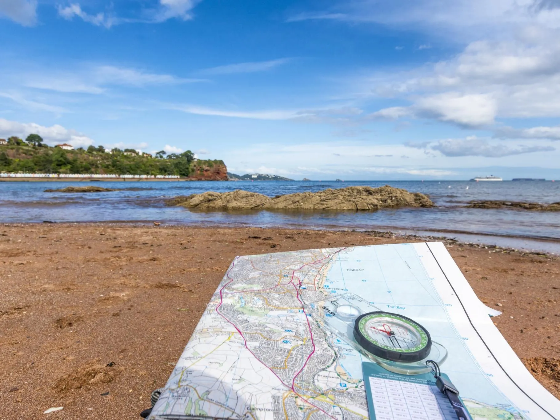 Ordnance Survey map and compass on a sandy beach beside the sea on the South West Coast Path