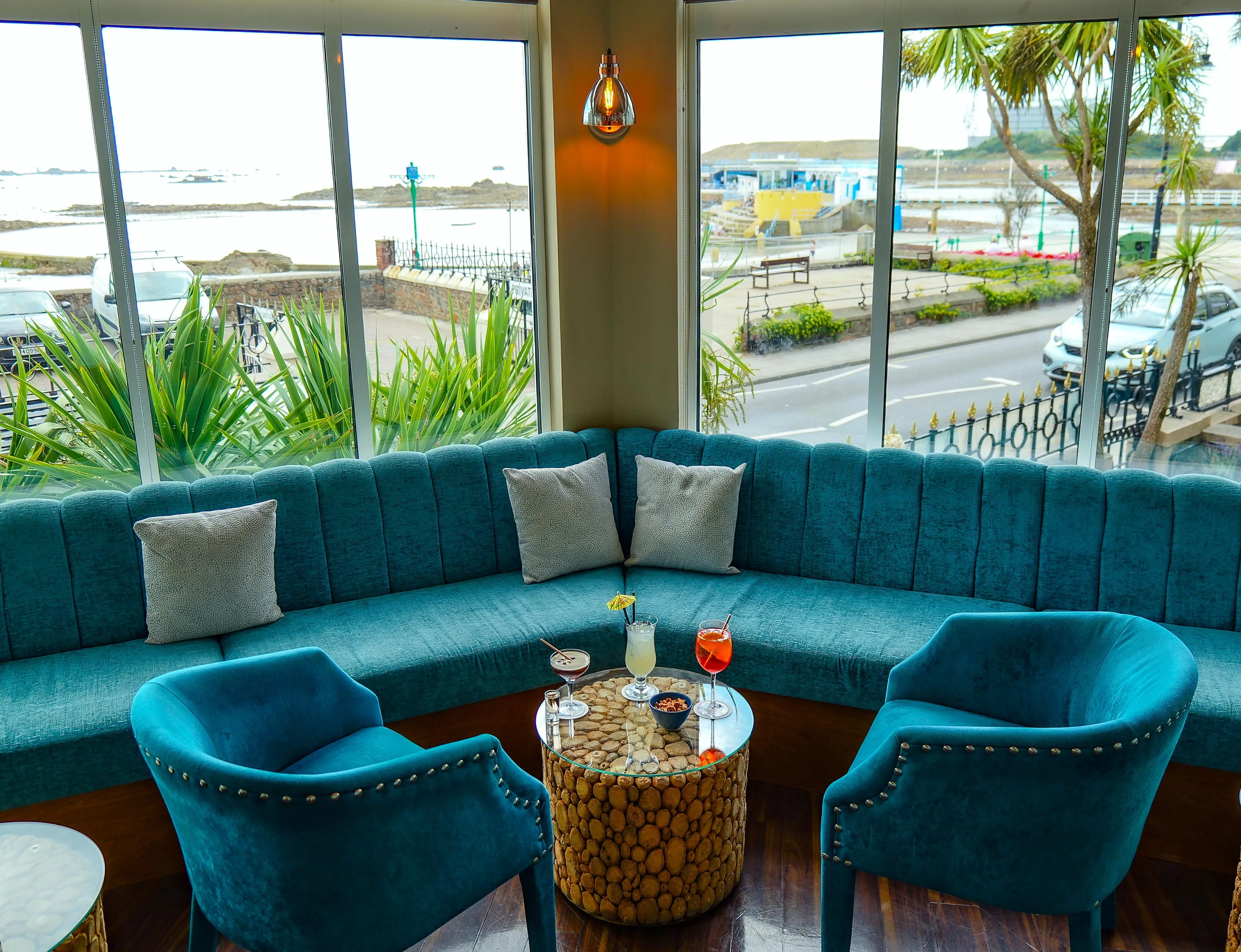 Stylish bar seating area with turquoise sofas and cocktails beside large windows overlooking the seafront
